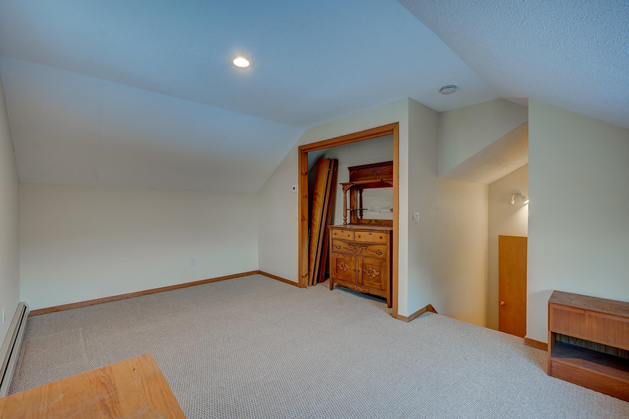 Carpeted upper-level room with a sloped ceiling, ornate wooden dresser, and open stairwell.