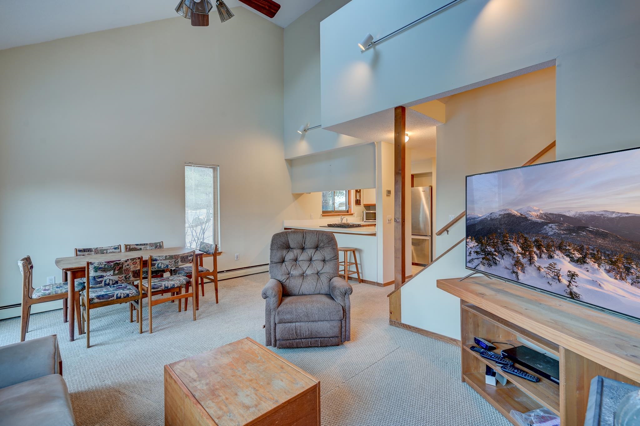 Living room with a vaulted ceiling, gray armchair, dining area, and open kitchen.
