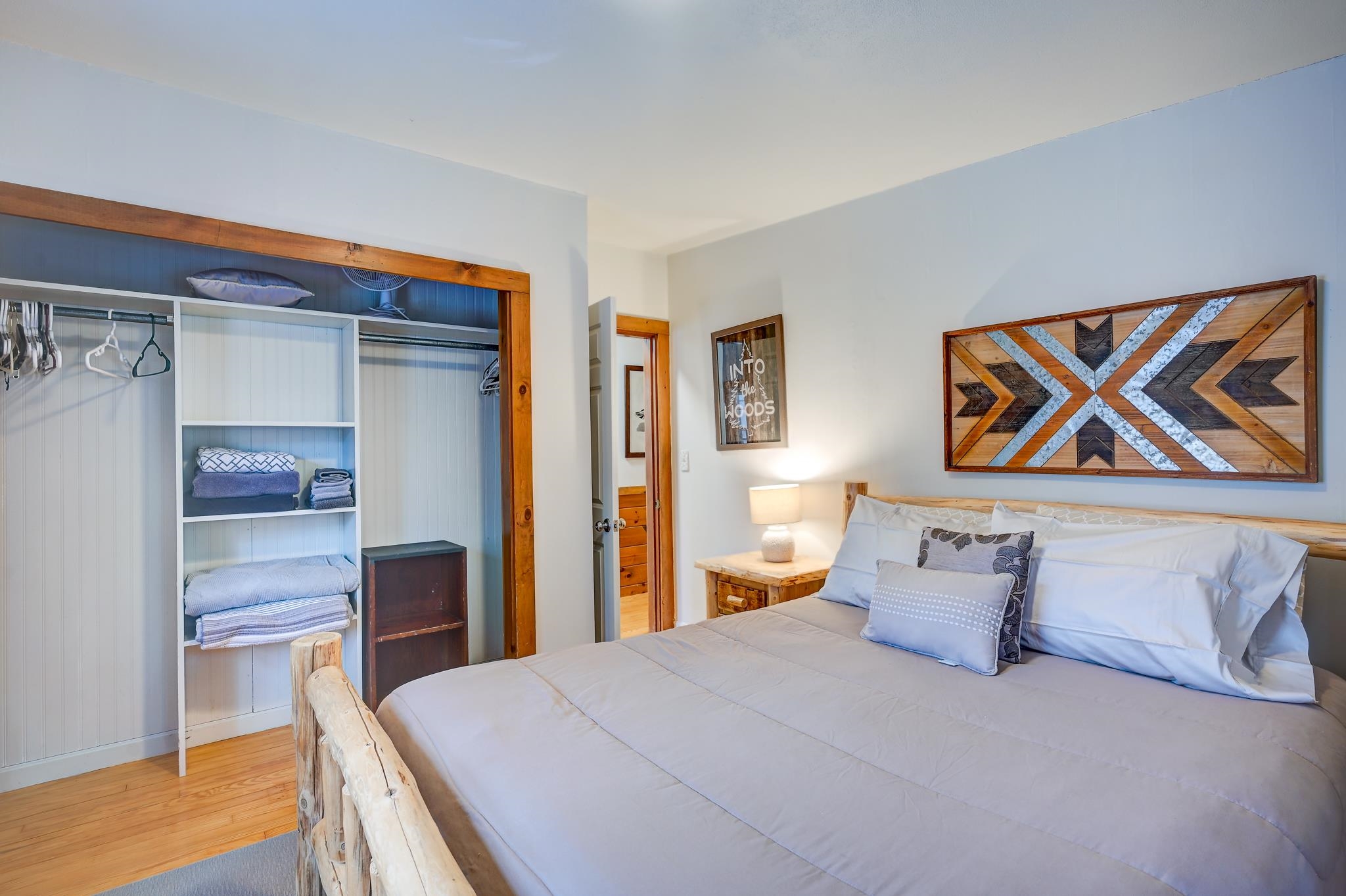 Bedroom with a log-style bed, geometric wood wall art, and an open closet with folded towels.