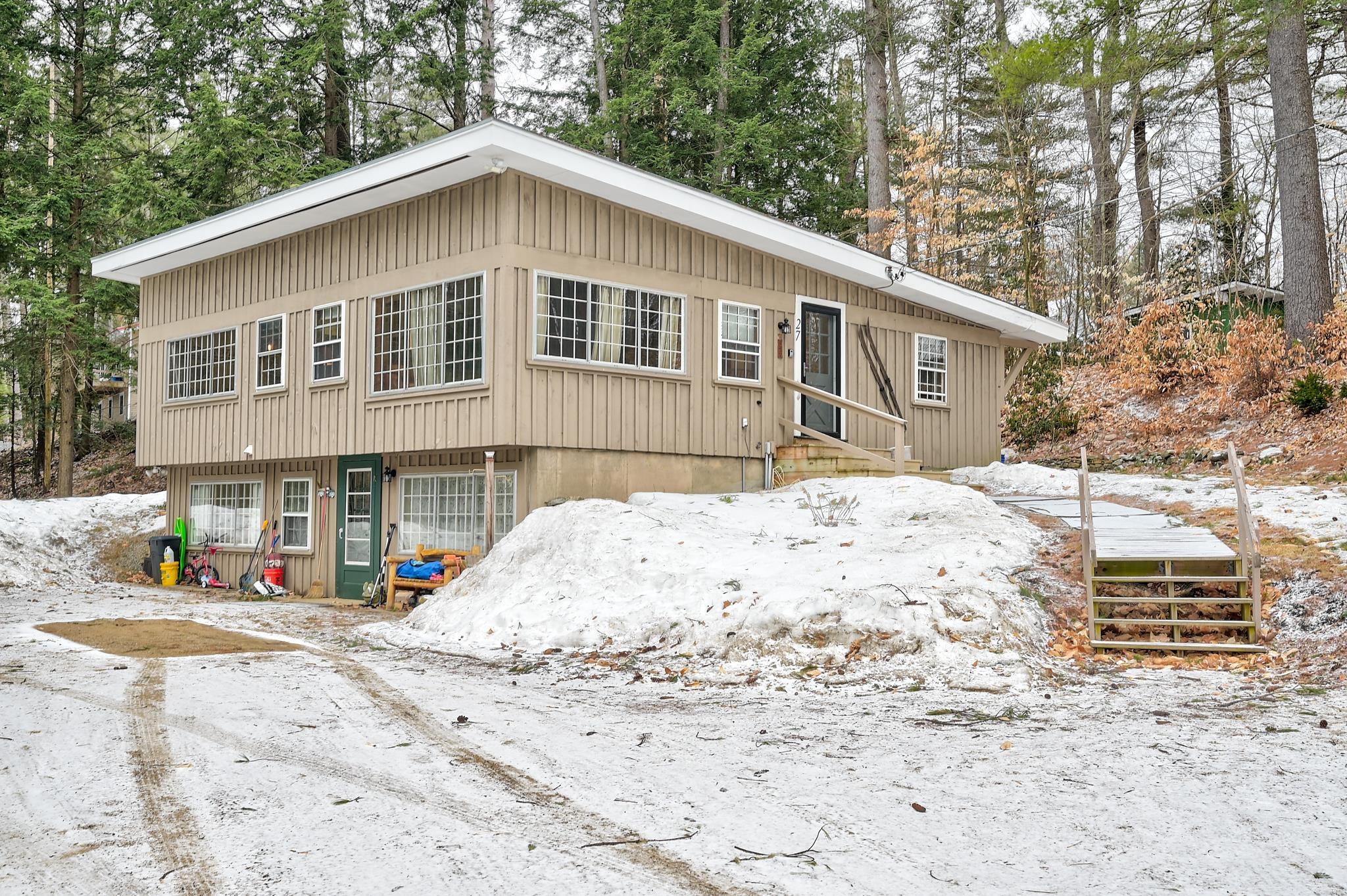 Beige split-level house with a broad gabled roof, snowy yard, and wooden steps to the entrance.