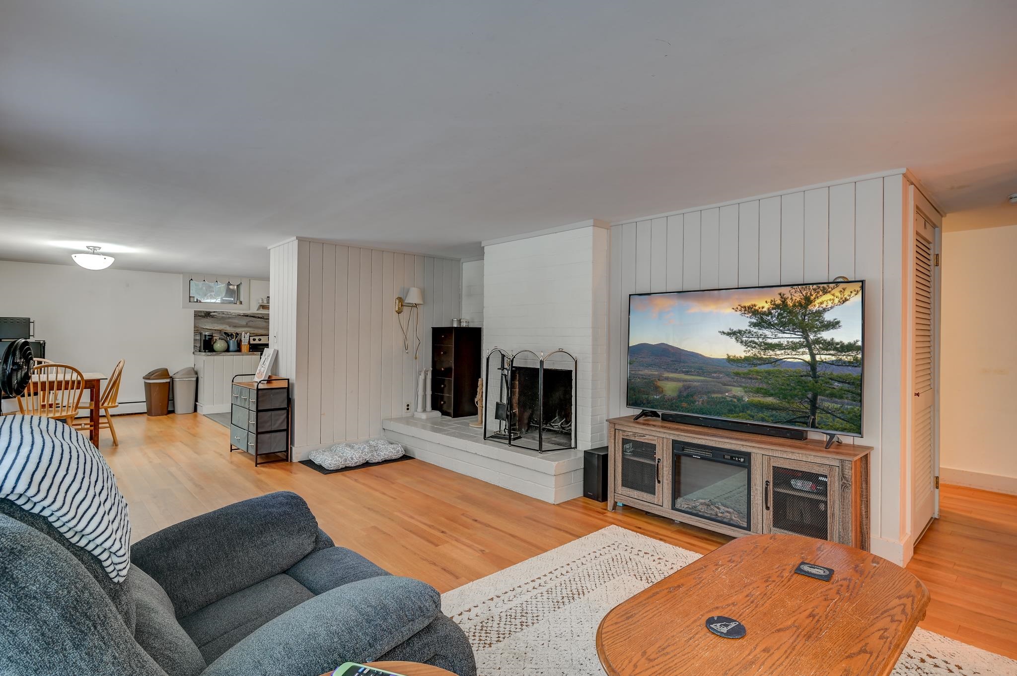 Living room with a gray sectional, white fireplace, and television beside a dining area.