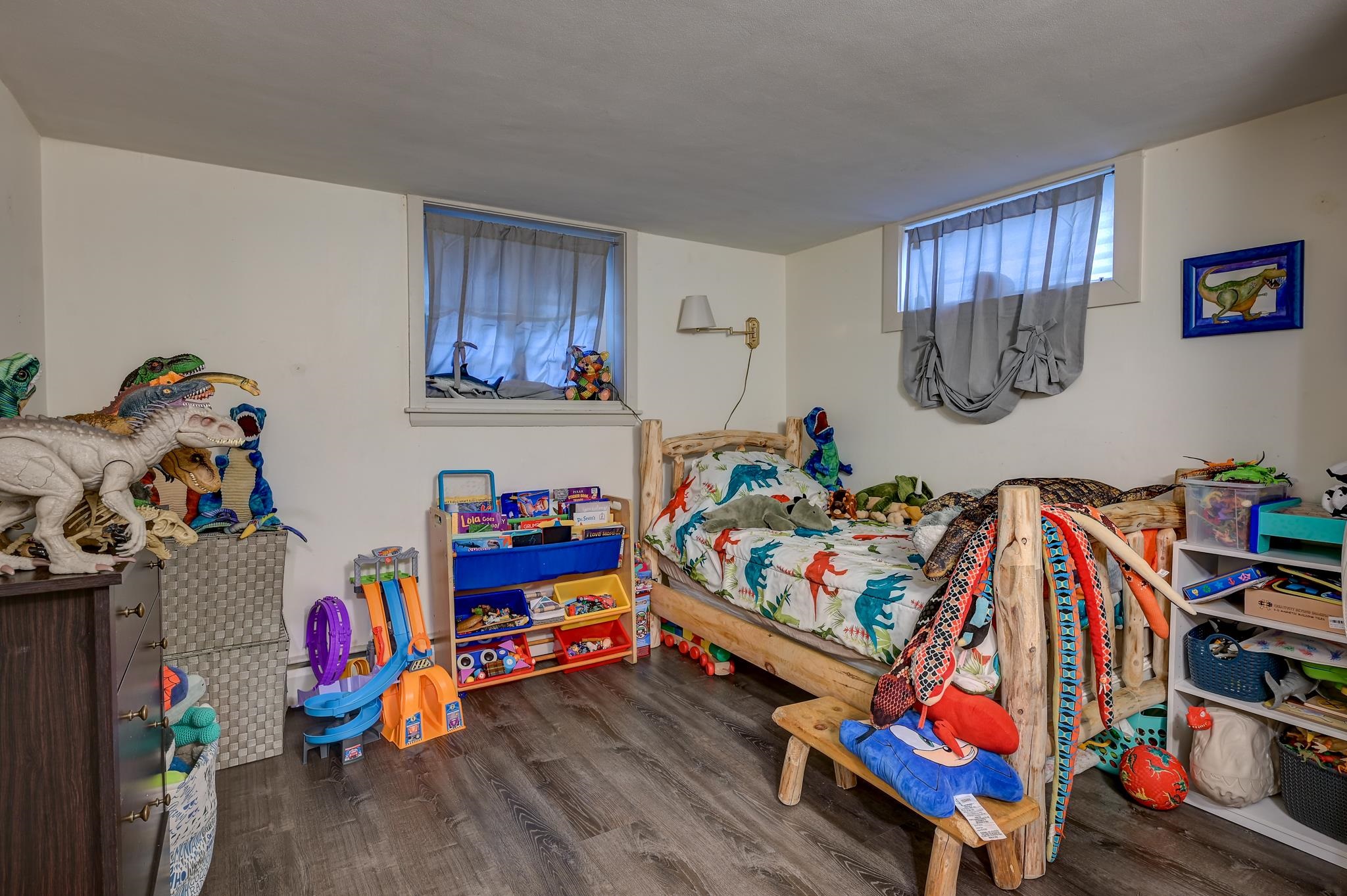 Children’s bedroom with rustic wooden beds, dinosaur bedding, and shelves crowded with toys.