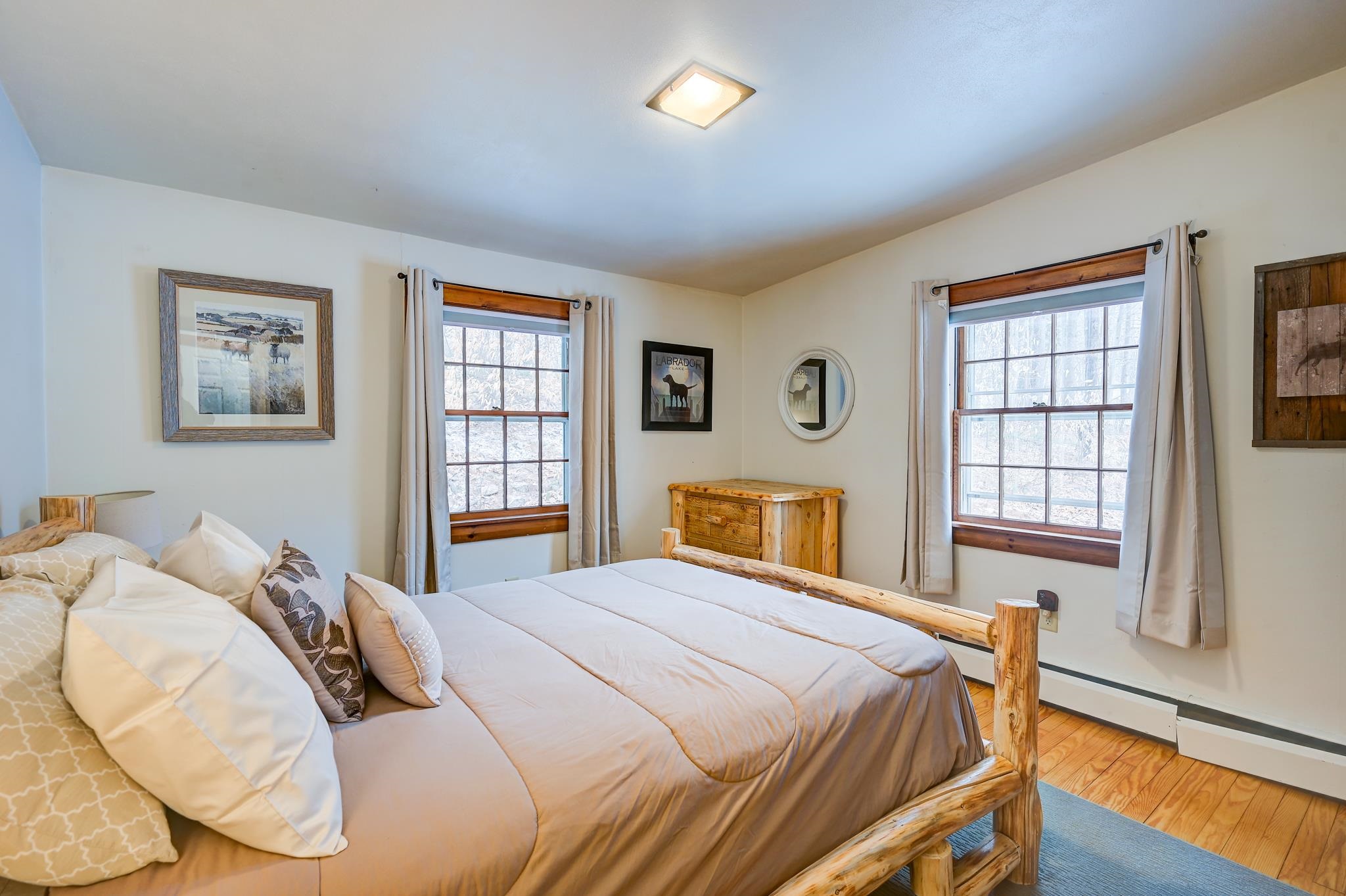 Bedroom with a rustic log bed, two curtained windows, and hardwood floors.