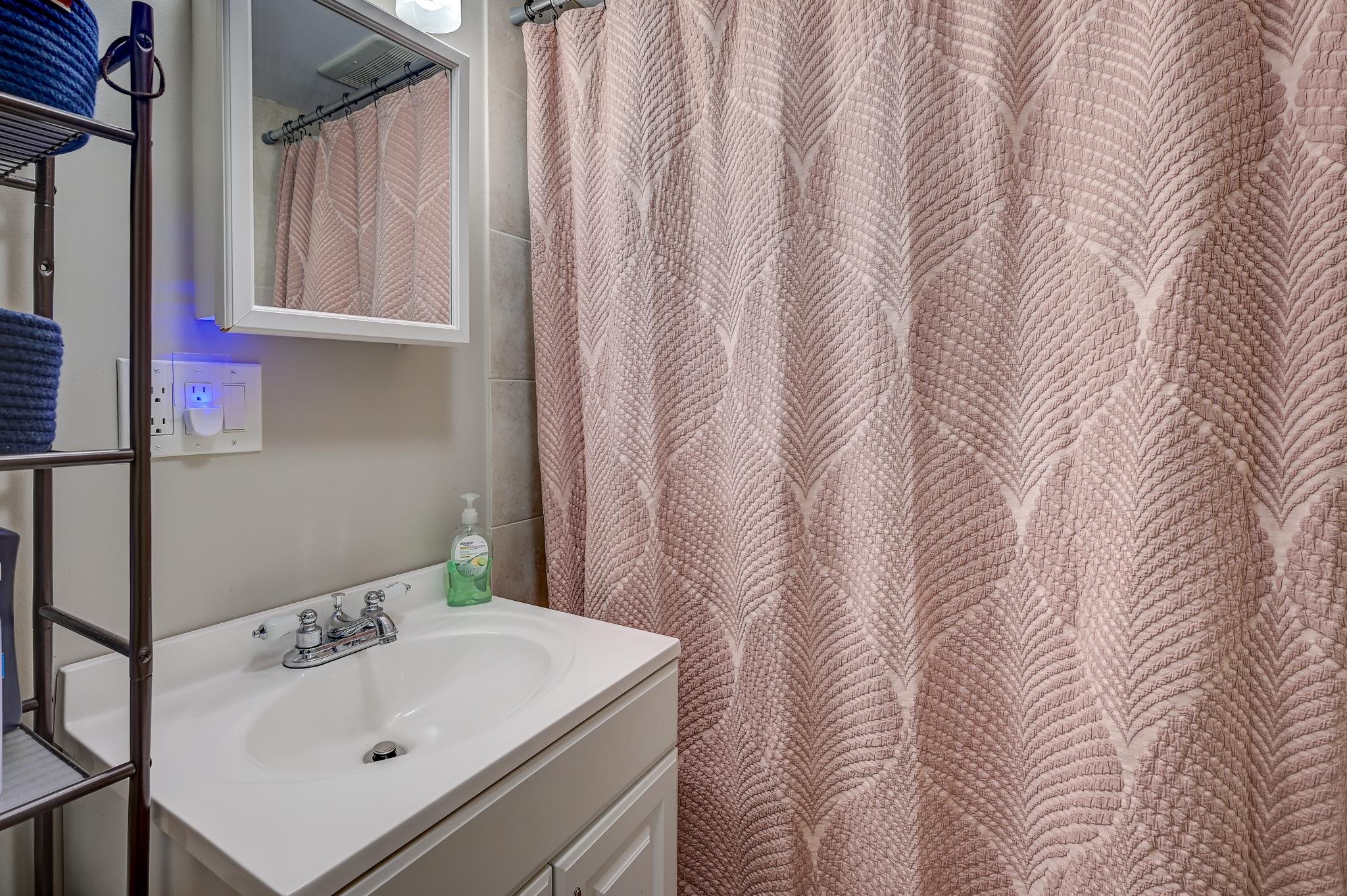 Bathroom sink and white vanity beside a pink patterned shower curtain.