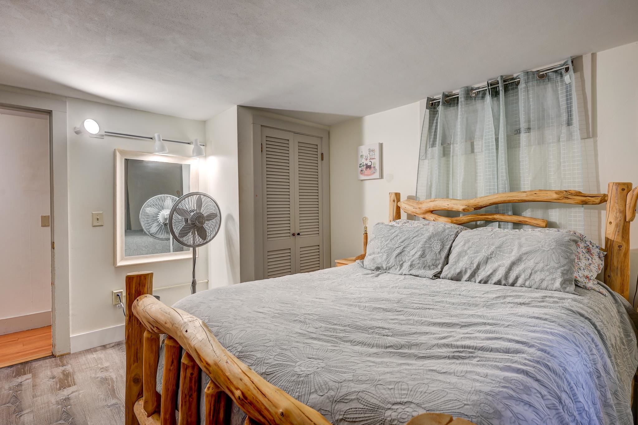Bedroom with a rustic log-frame bed, gray floral bedding, and a standing fan.