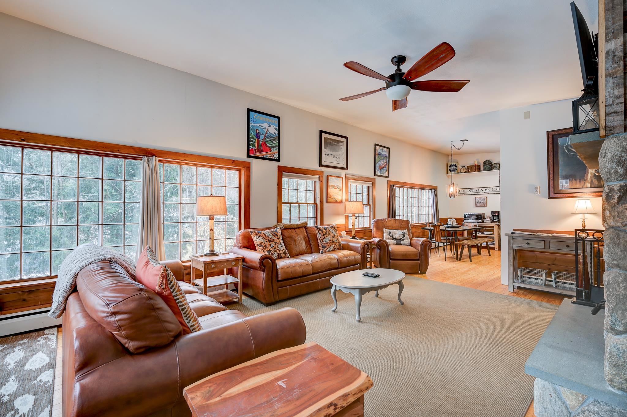 Living room with leather seating, a stone fireplace, and large wood-trimmed windows.