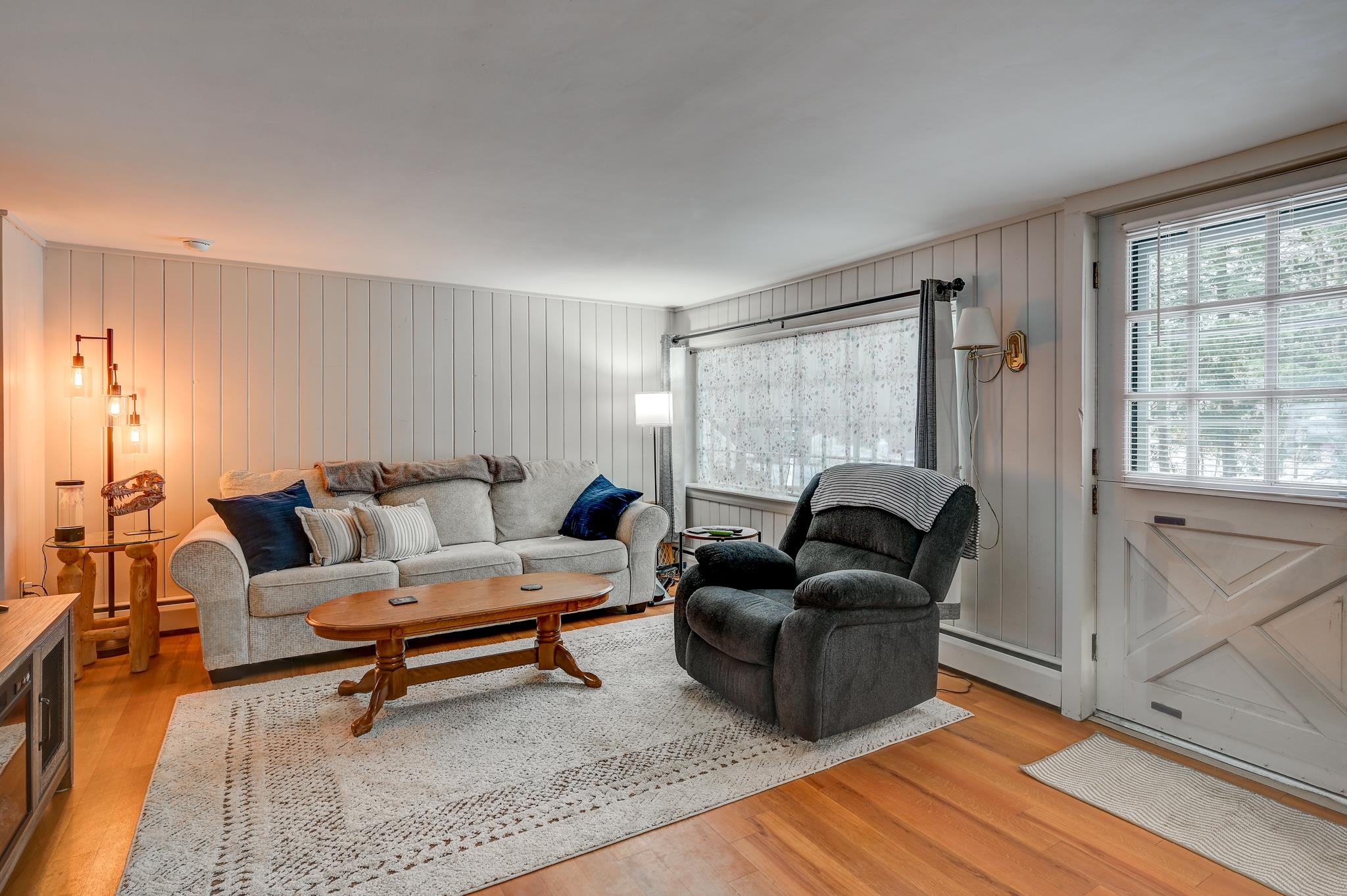 Living room with a light sofa, dark recliner, wood coffee table, and large windows.