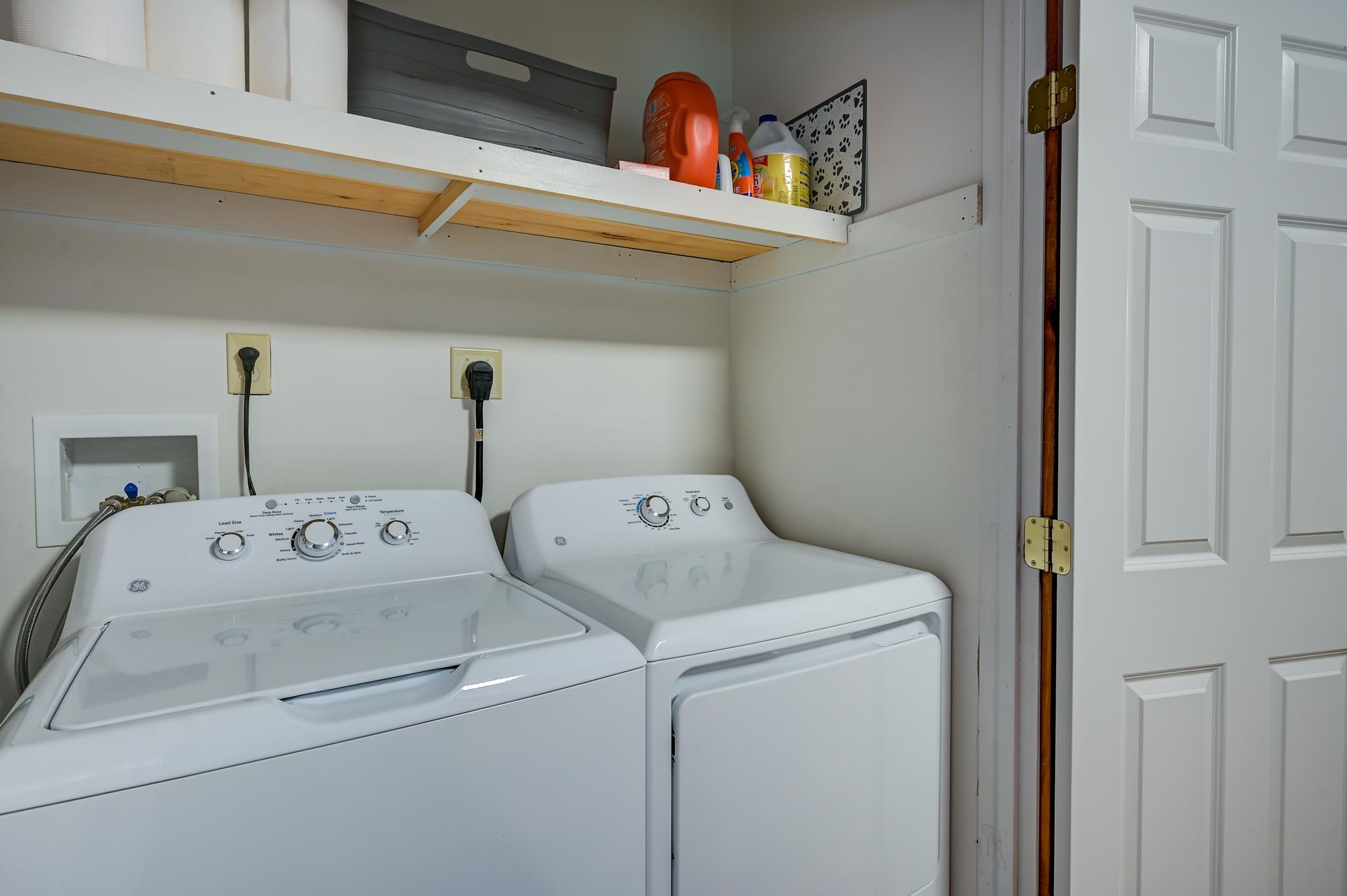 Laundry room with a white washer and dryer beneath wall-mounted shelves.