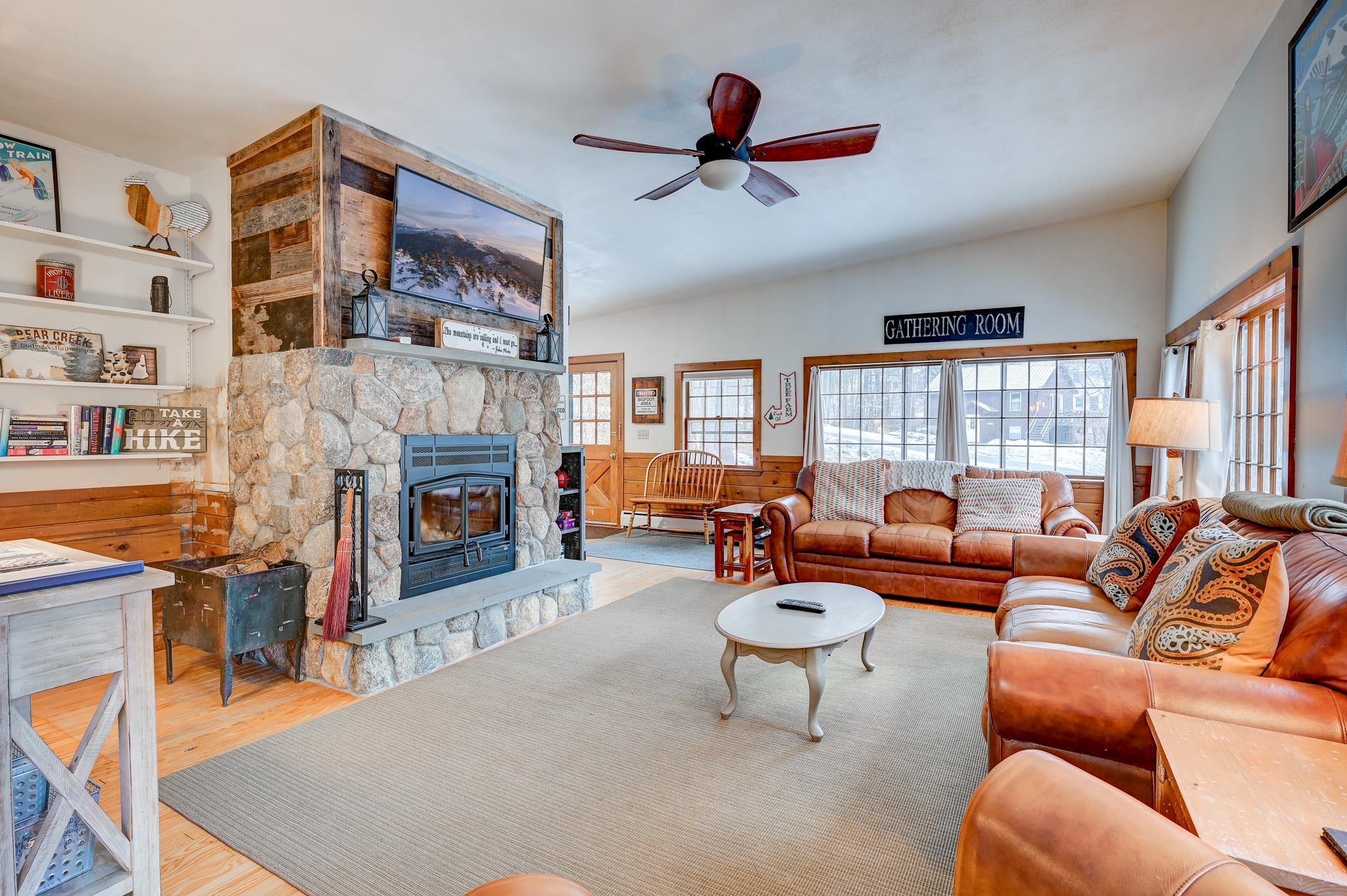 Living room with a stone fireplace, leather sofas, and large windows overlooking snow.