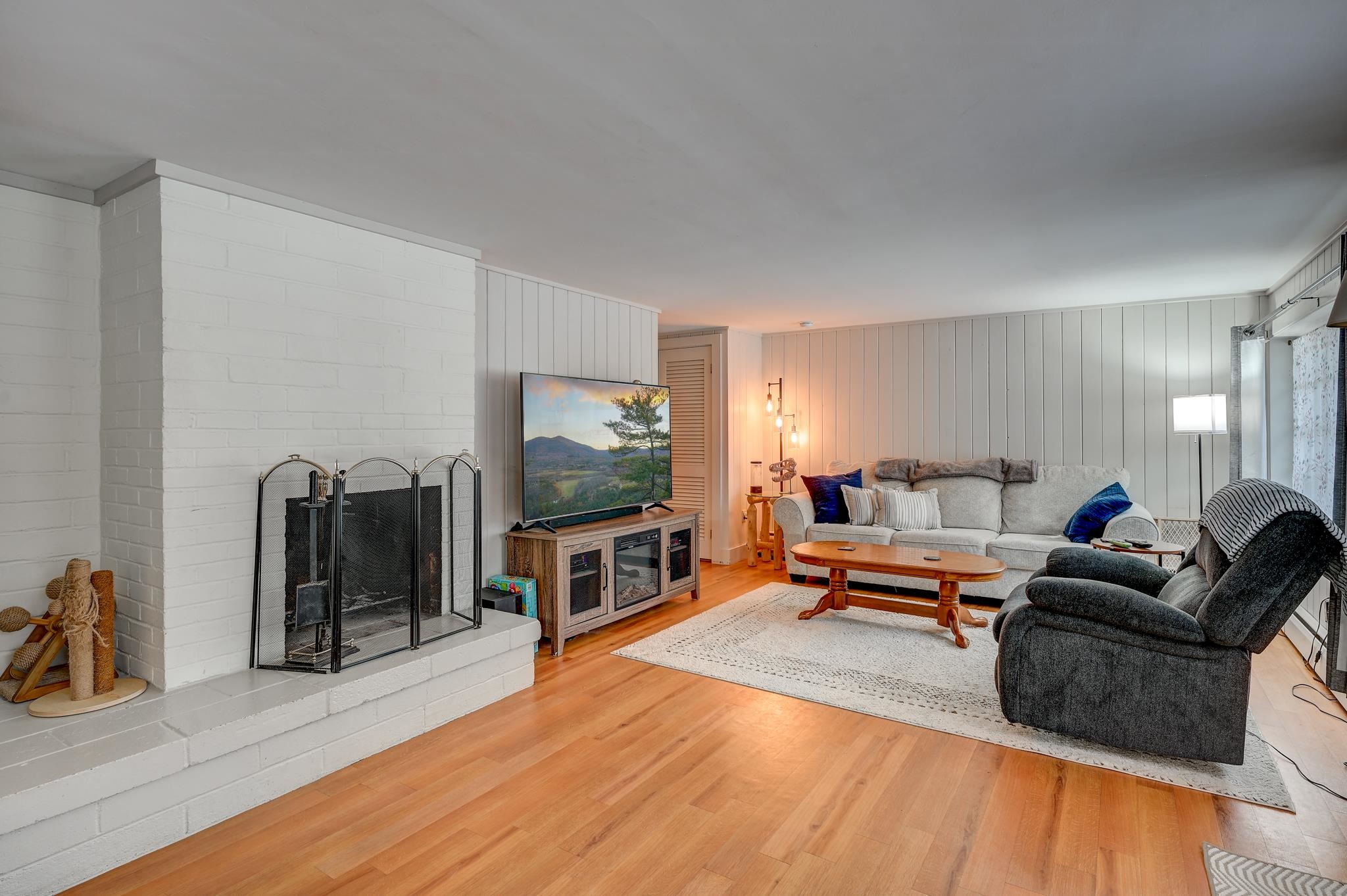 Living room with white brick fireplace, gray seating, and warm wood floors.