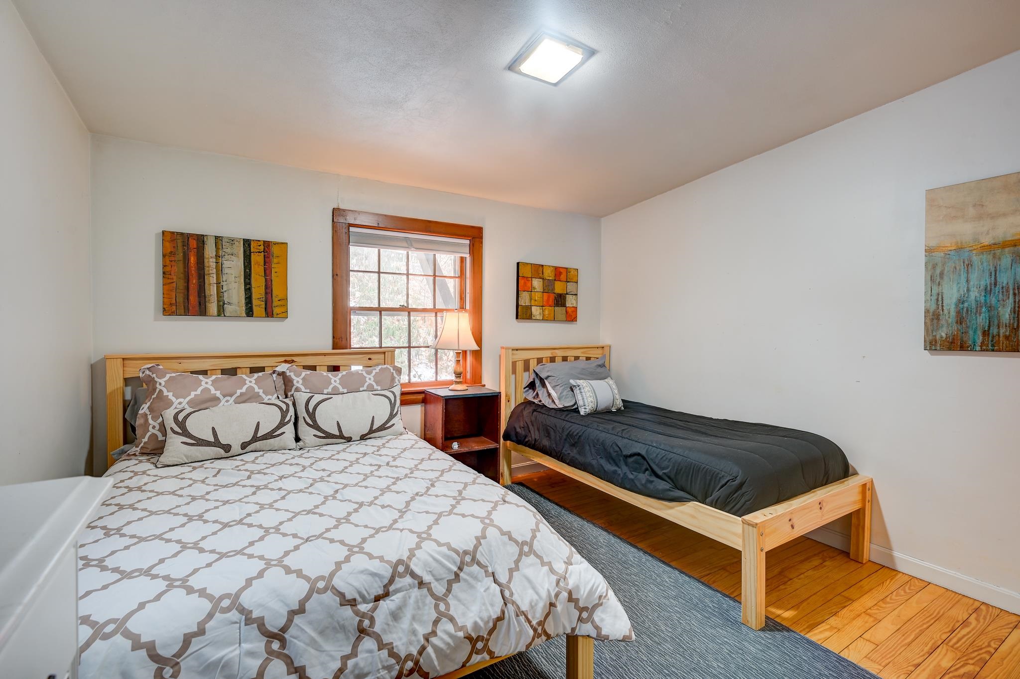 Bedroom with a double bed, single bed, wood-trimmed window, and hardwood floors.