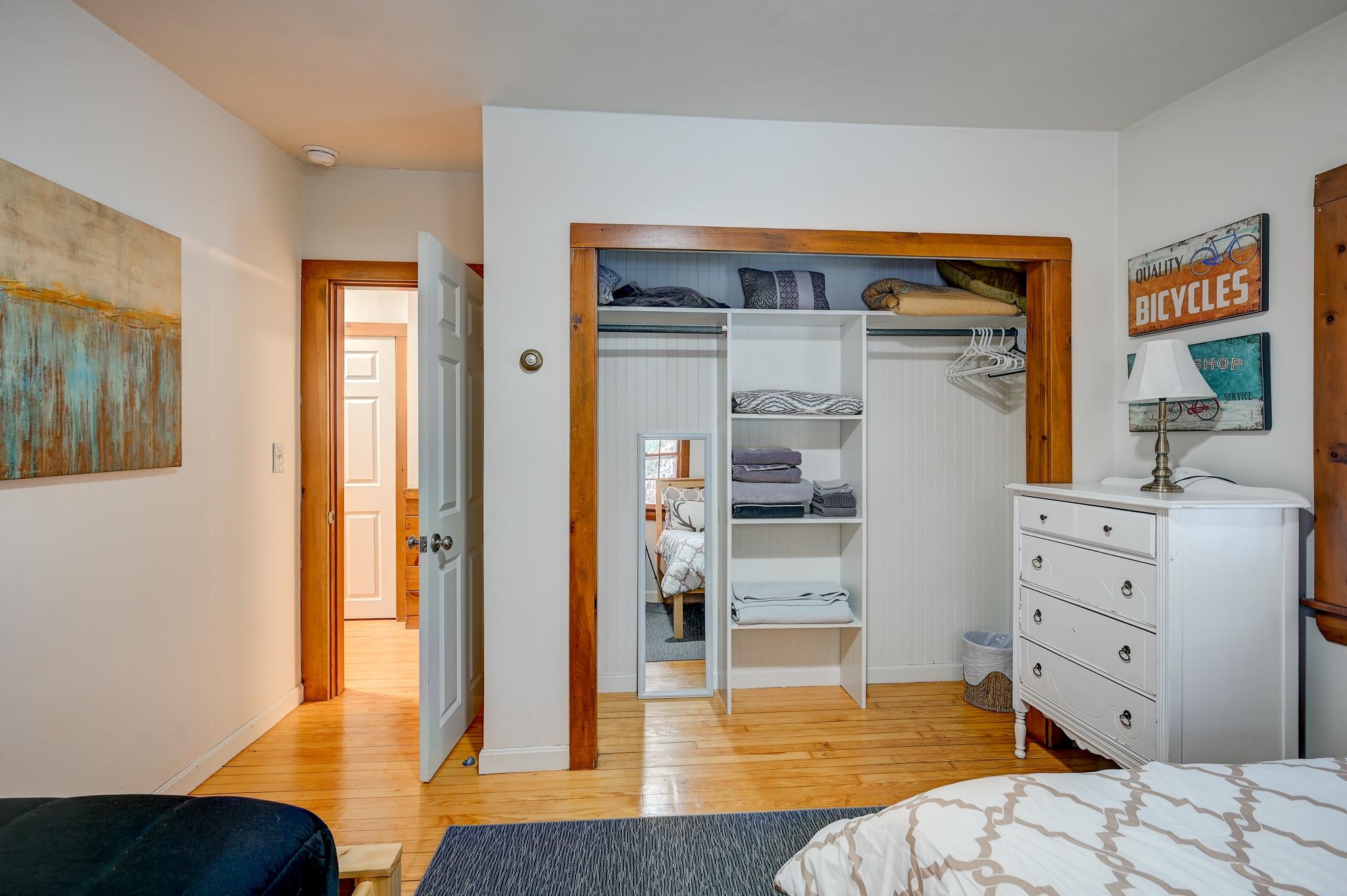 Bedroom with an open, organized closet, folded linens, a full-length mirror, and a white dresser.