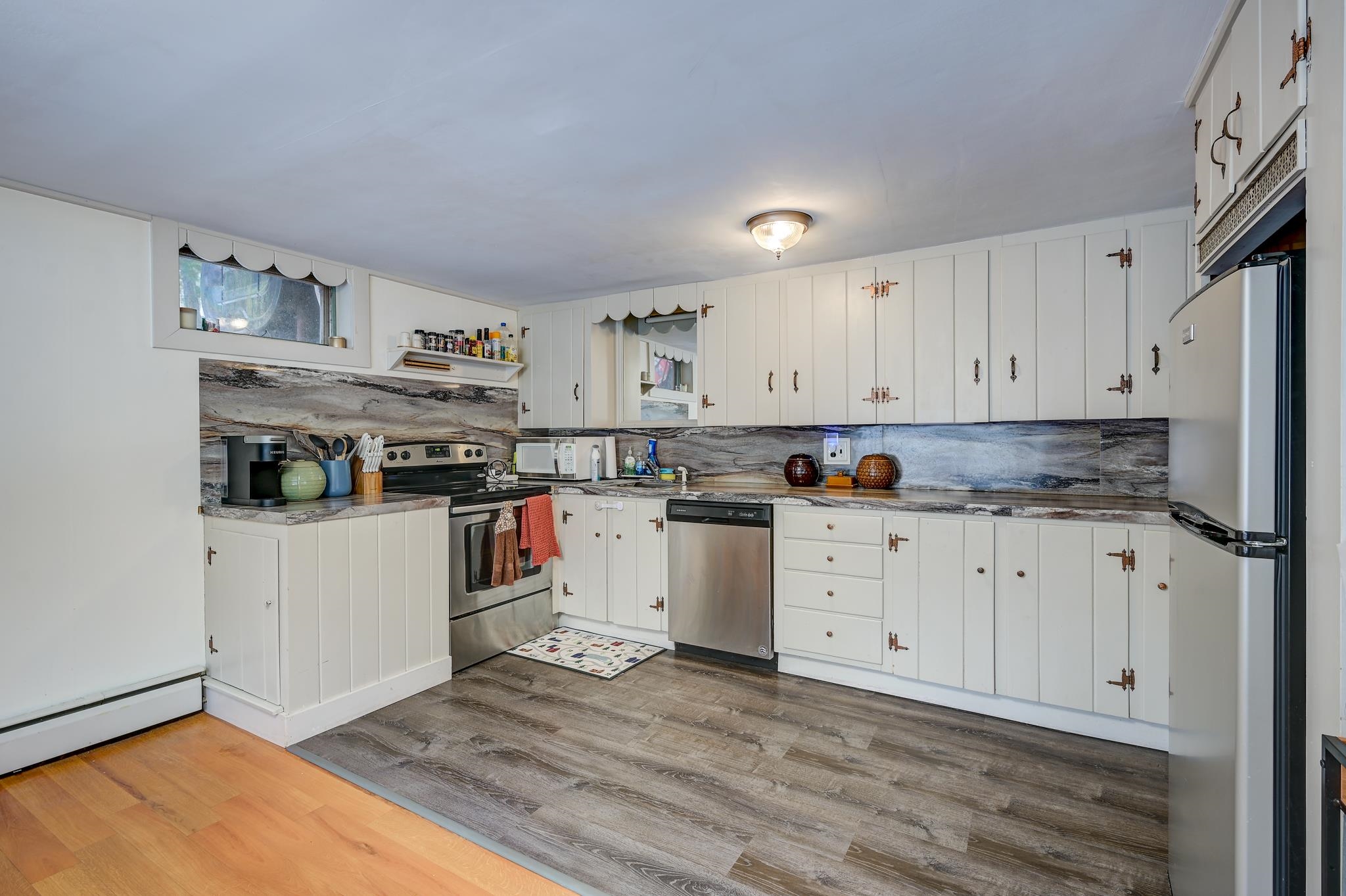 Kitchen with white cabinets, gray stone-patterned counters, stainless steel appliances, and mixed wood flooring.