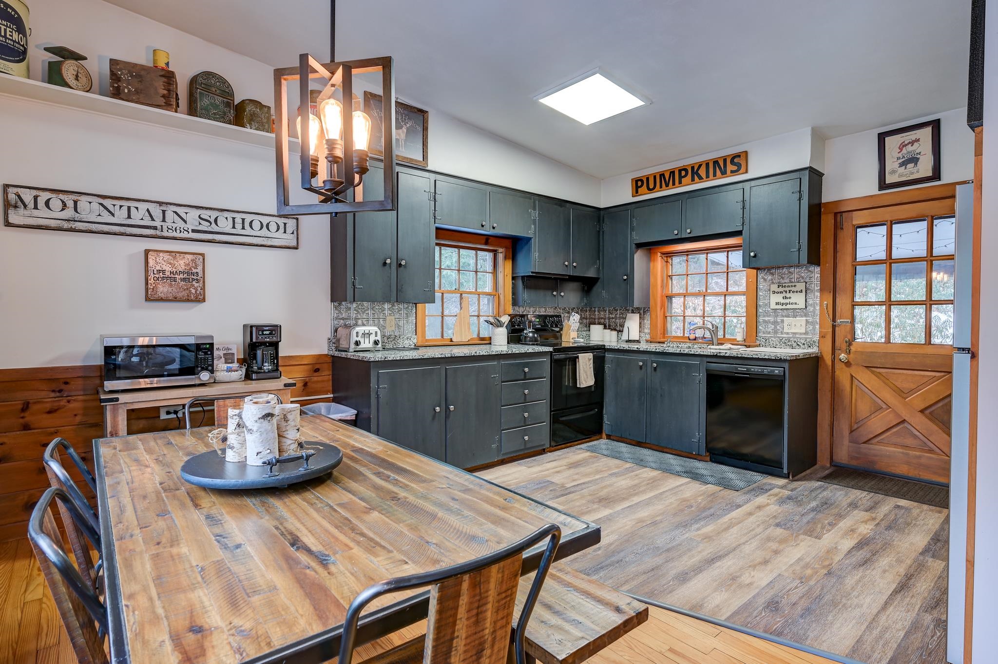 Kitchen with dark blue-gray cabinets, patterned tile backsplash, rustic dining table, and wood-trimmed windows.