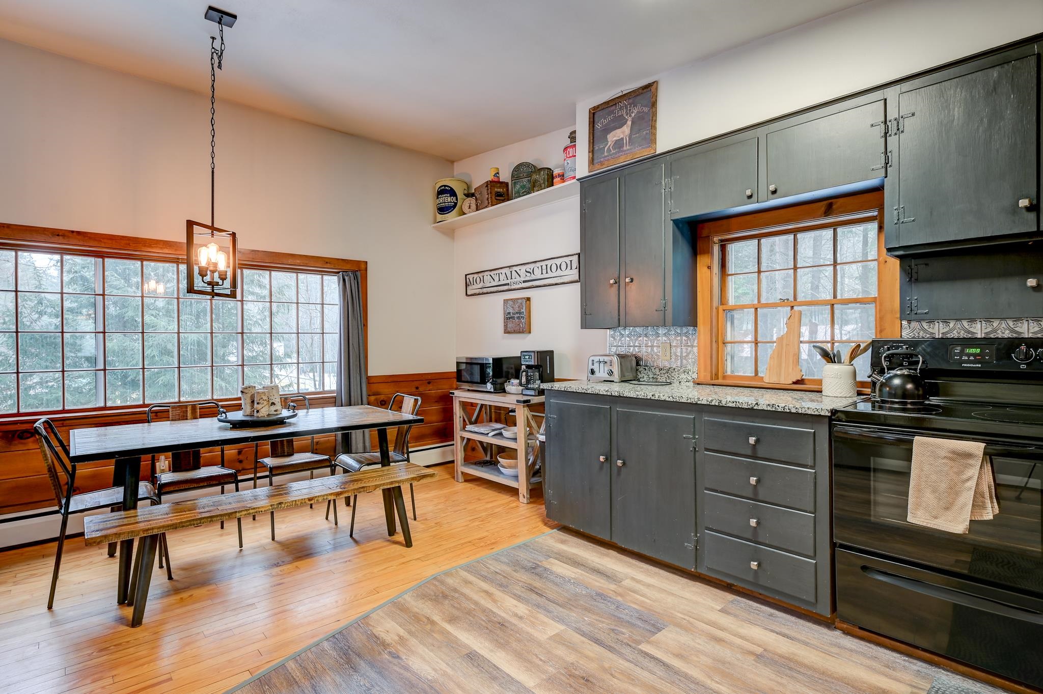 Kitchen and dining area with gray cabinets, granite counters, and large wood-trimmed windows overlooking snowy trees.