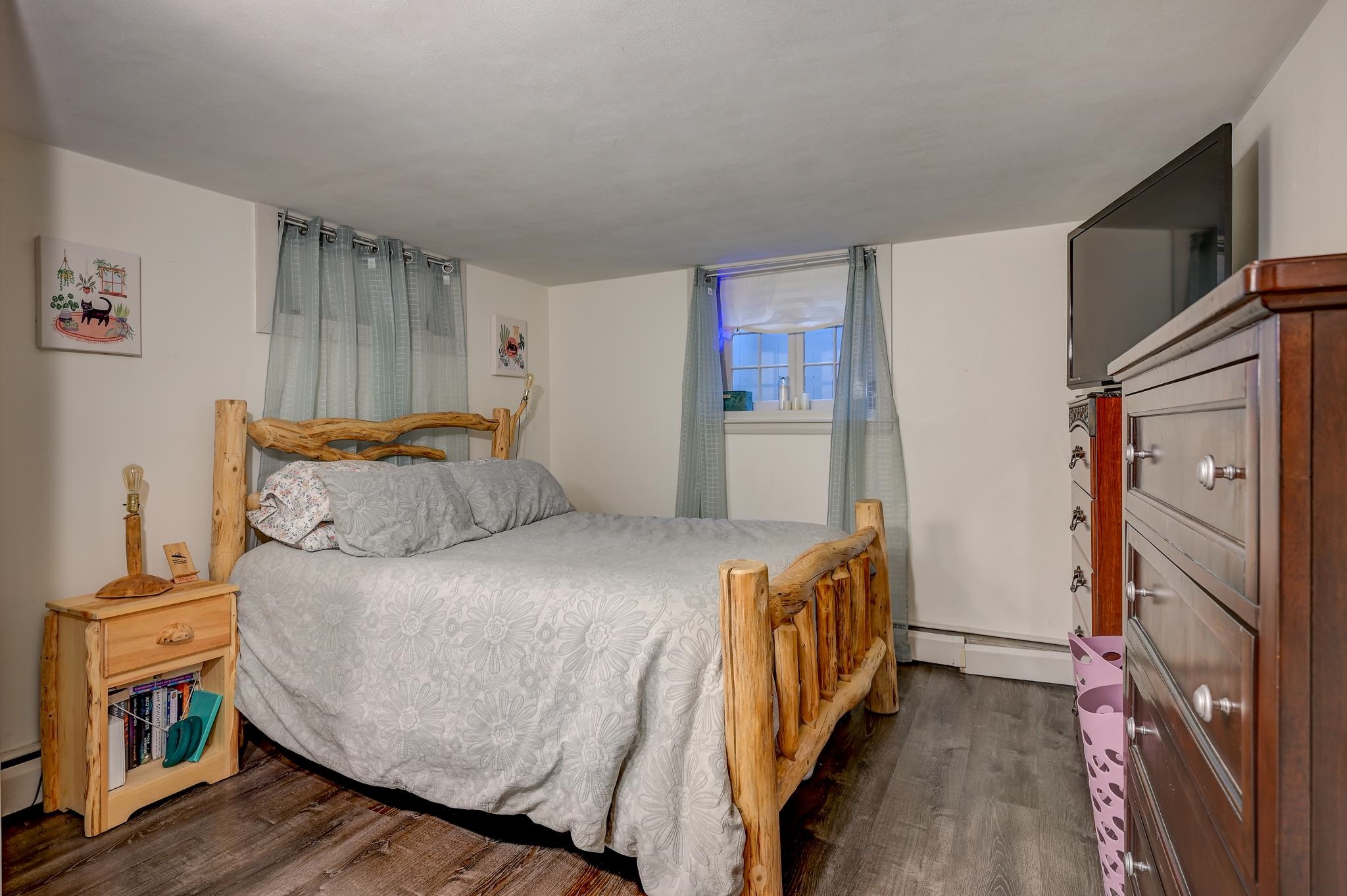 Bedroom with a rustic log-frame bed, gray floral bedding, and a curtained window.