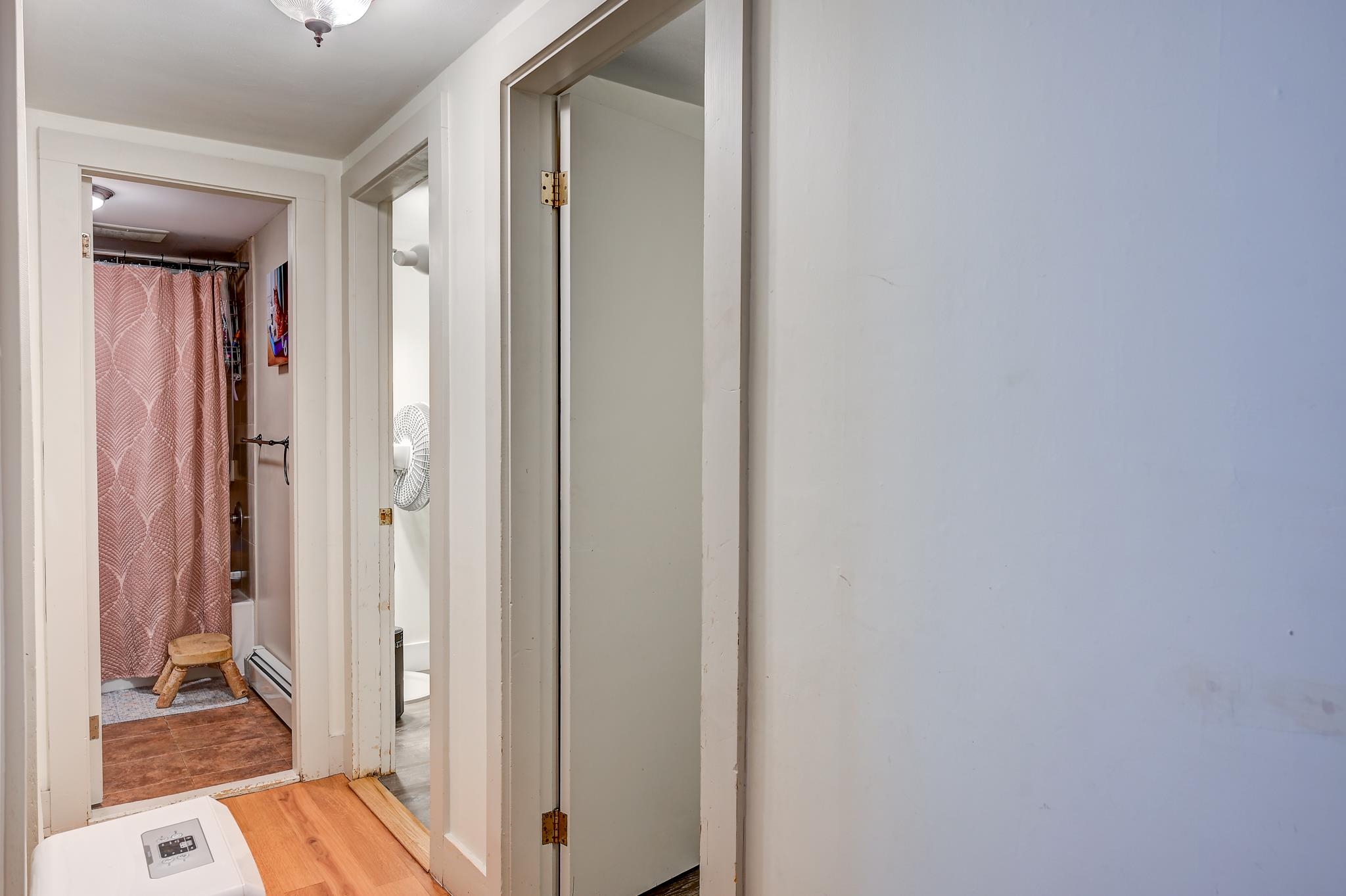 Hallway with wood flooring, open doorways, and a bathroom with a pink patterned shower curtain.