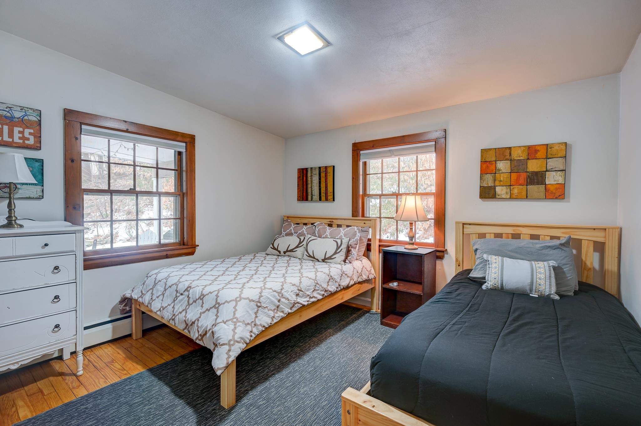 Bedroom with two single beds, warm wood window trim, hardwood floors, and snow visible outside.