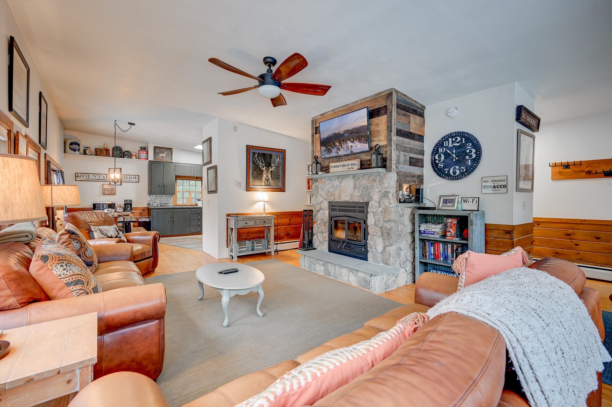 Living room with a large stone fireplace, leather sofas, and an open kitchen area.