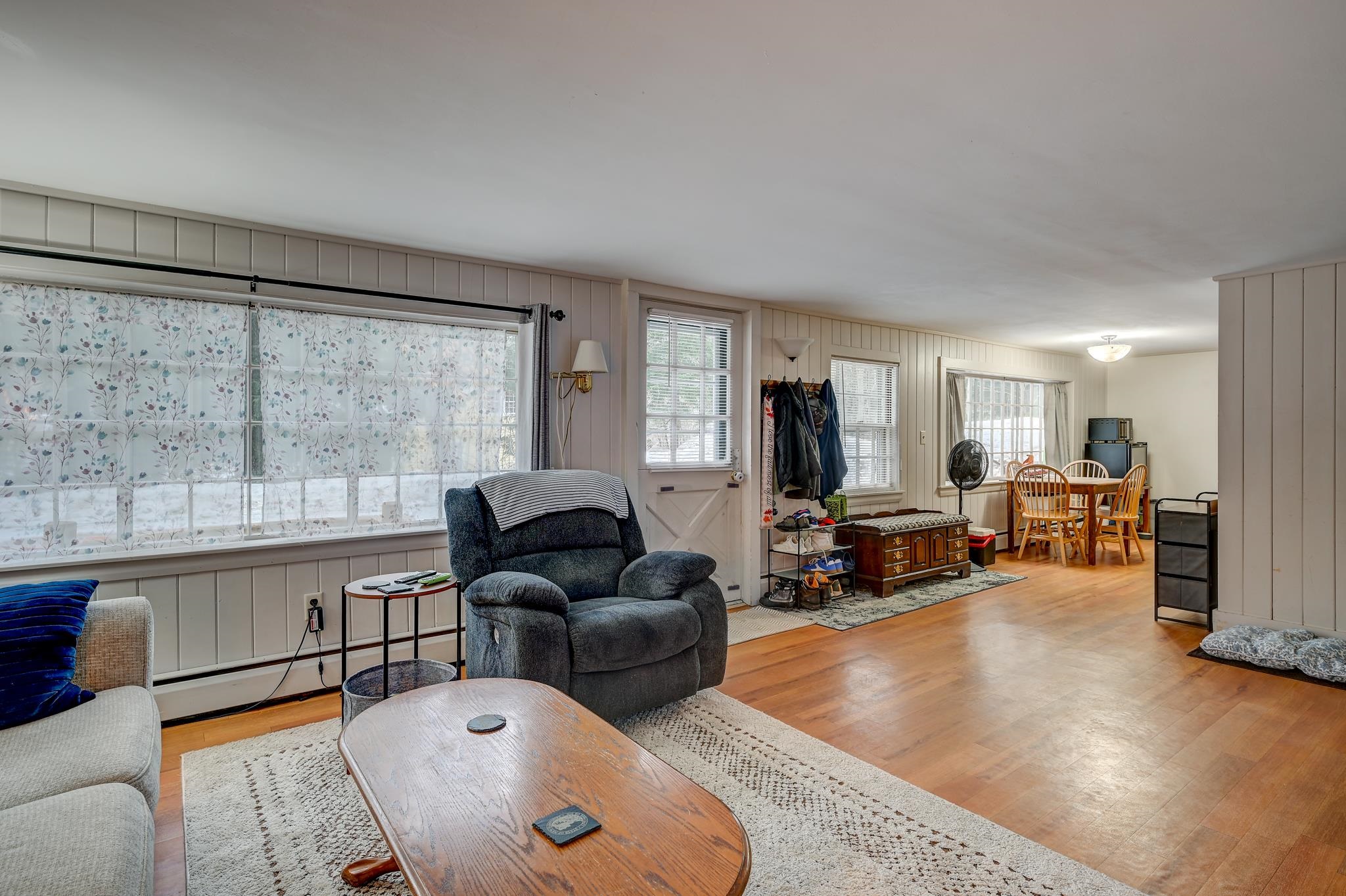 Living room with floral curtains, a gray recliner, wood floors, and an adjoining dining area.
