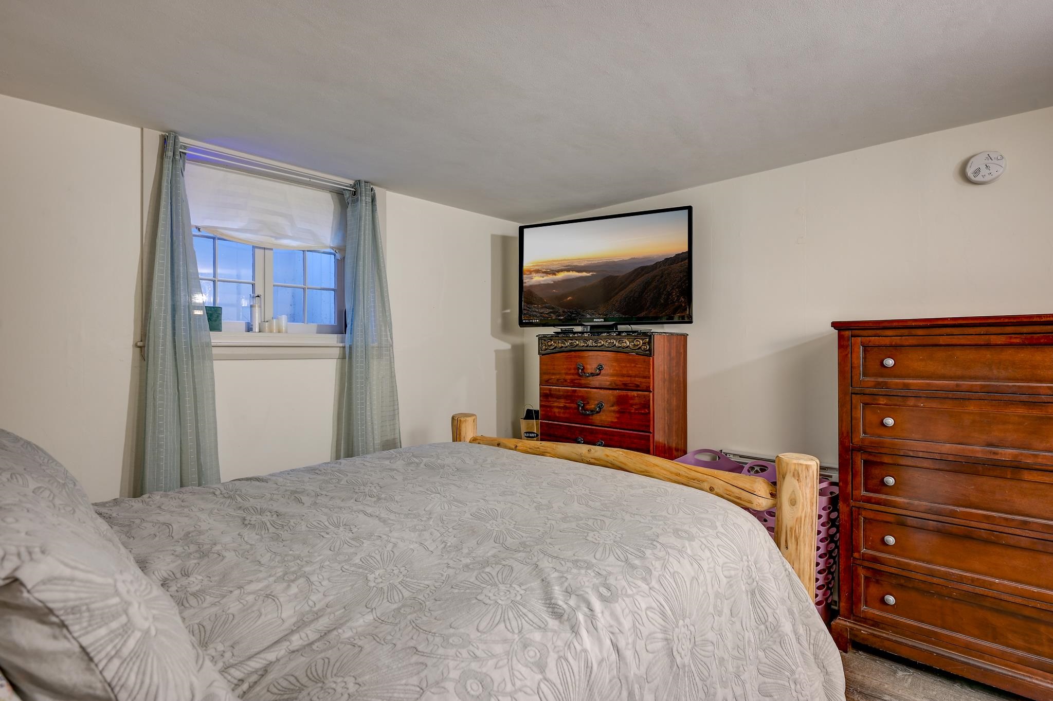 Furnished bedroom with gray floral bedding, wooden dressers, and a television.