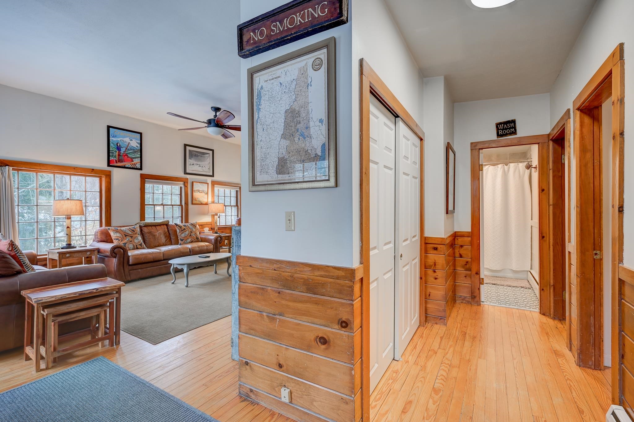 Living room and hallway with leather sofas, warm wood floors, and a bathroom at the end.
