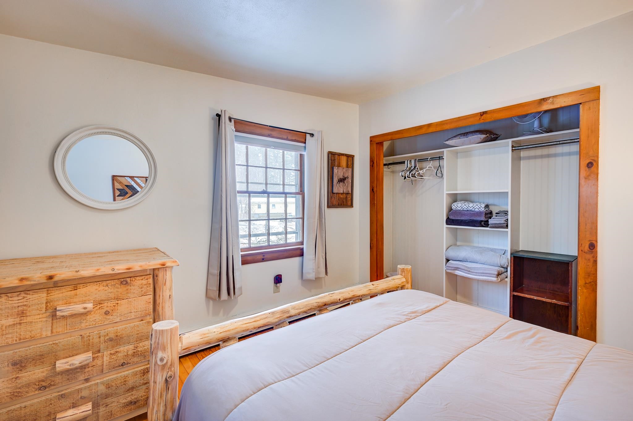 Bedroom with a rustic log-style bed, wooden dresser, and open closet with folded linens.