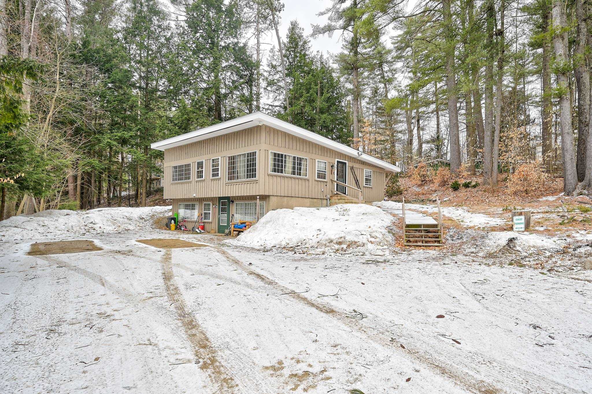 Tan split-level home with broad windows and a wooden entrance stairway on a snowy, wooded lot.
