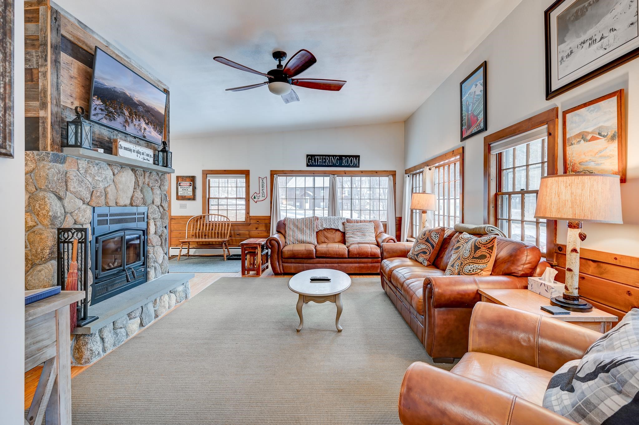 Furnished living room with a stone fireplace, leather sofas, and snowy views through large windows.