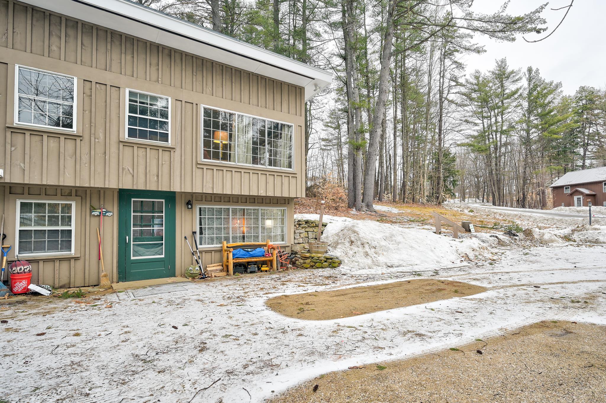 Tan split-level home with a green entrance door and patchy snow across the driveway.