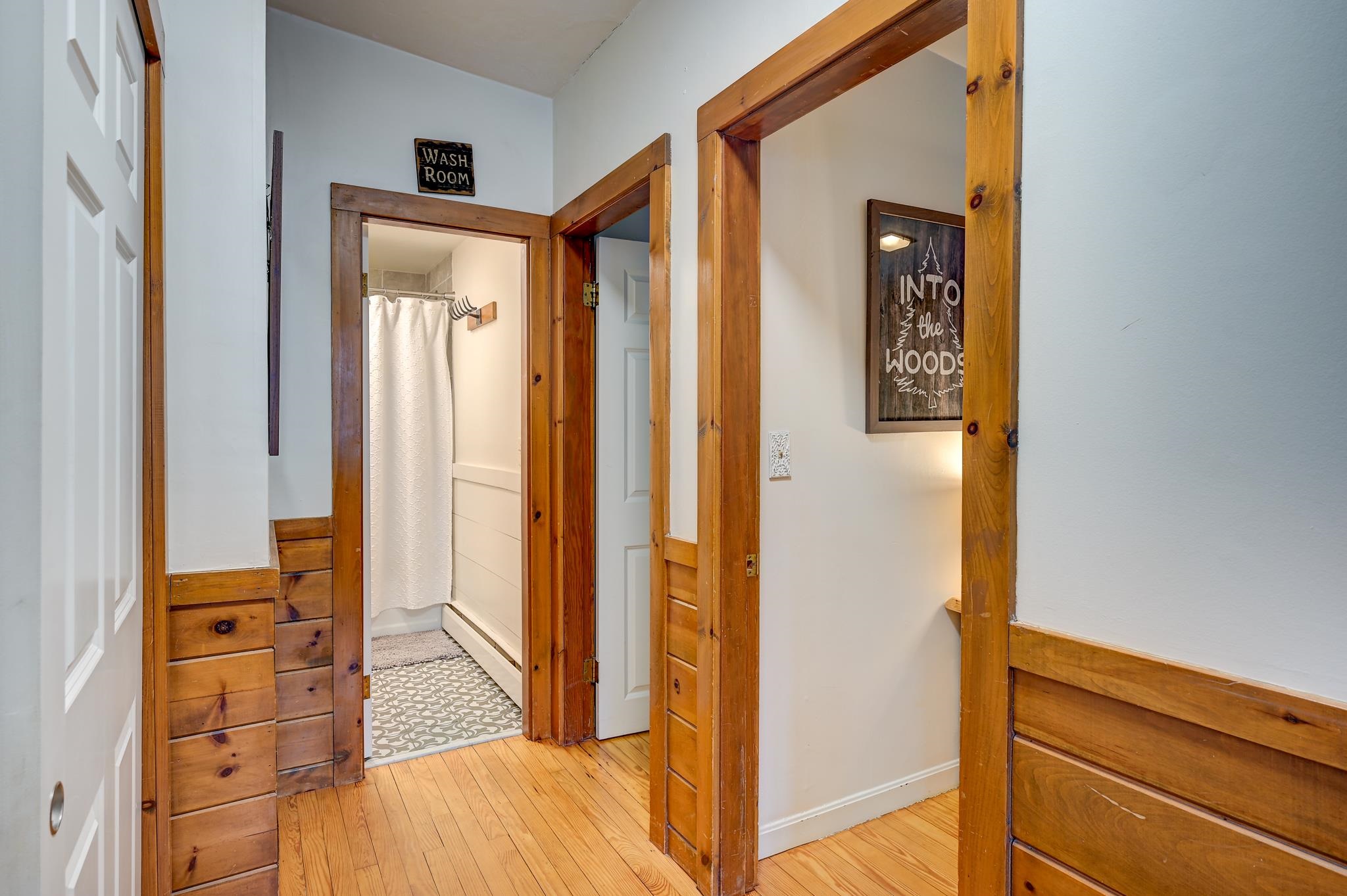 Wood-trimmed hallway with a bathroom doorway, white shower curtain, and patterned tile floor.