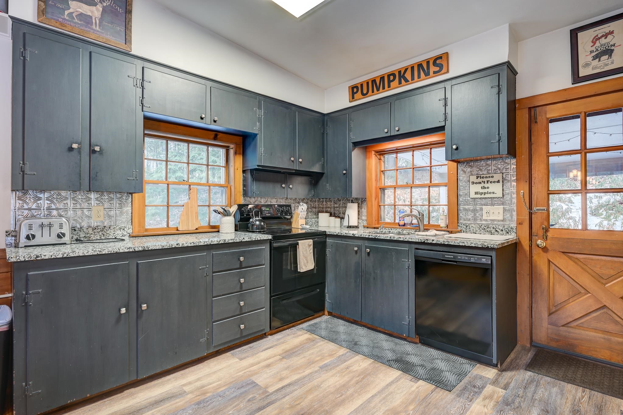 Kitchen with dark cabinets, granite counters, patterned backsplash, and warm wood-trimmed windows.