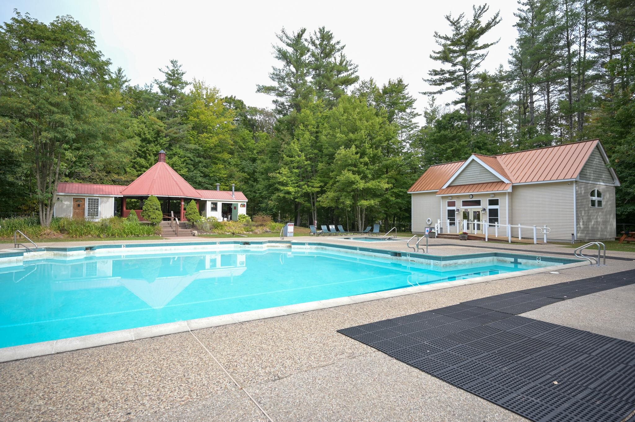 Outdoor pool beside a red-roofed pavilion and pool building, surrounded by trees.