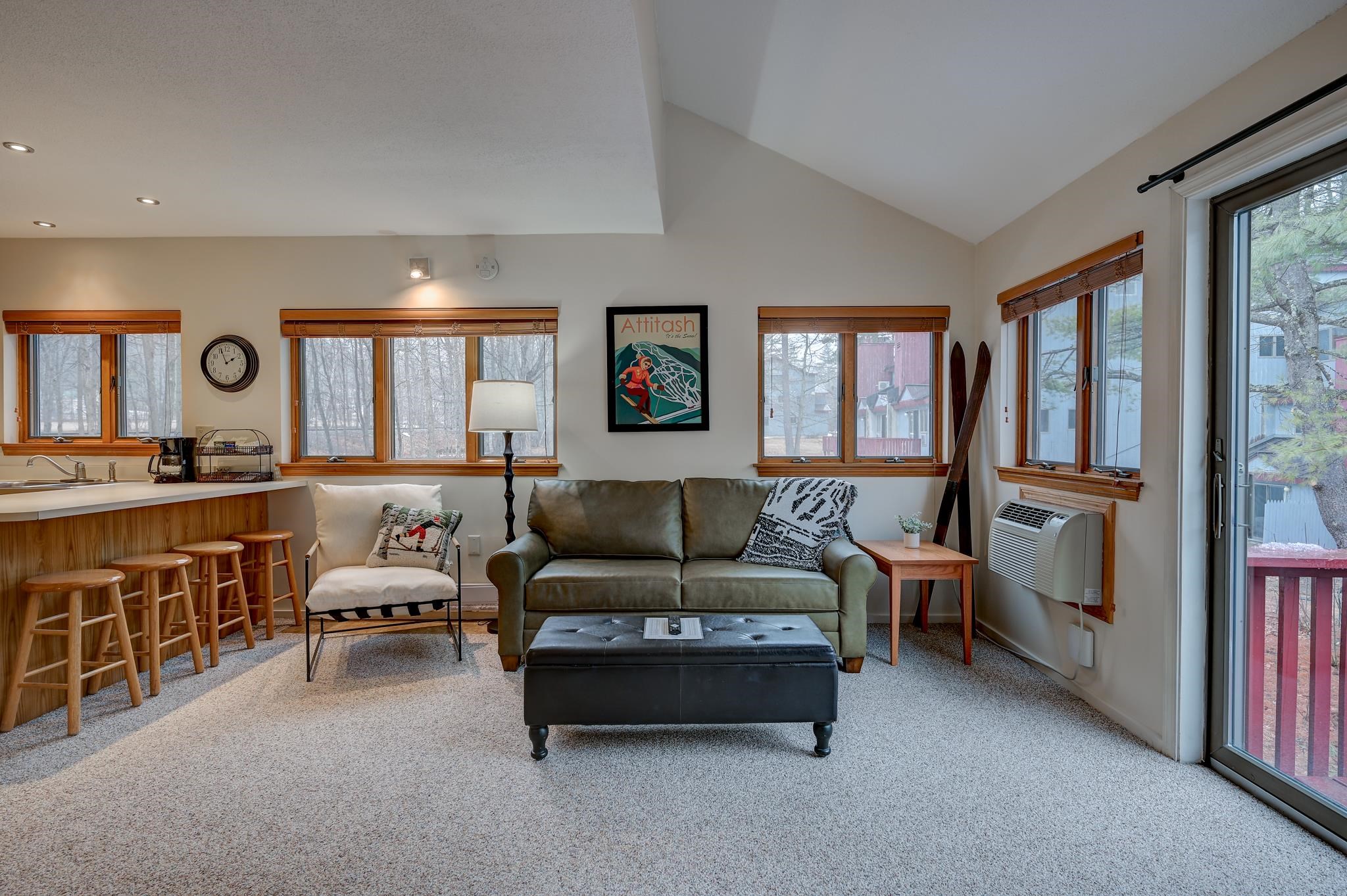 Living room with a green sofa, breakfast bar, vaulted ceiling, and wood-trimmed windows.