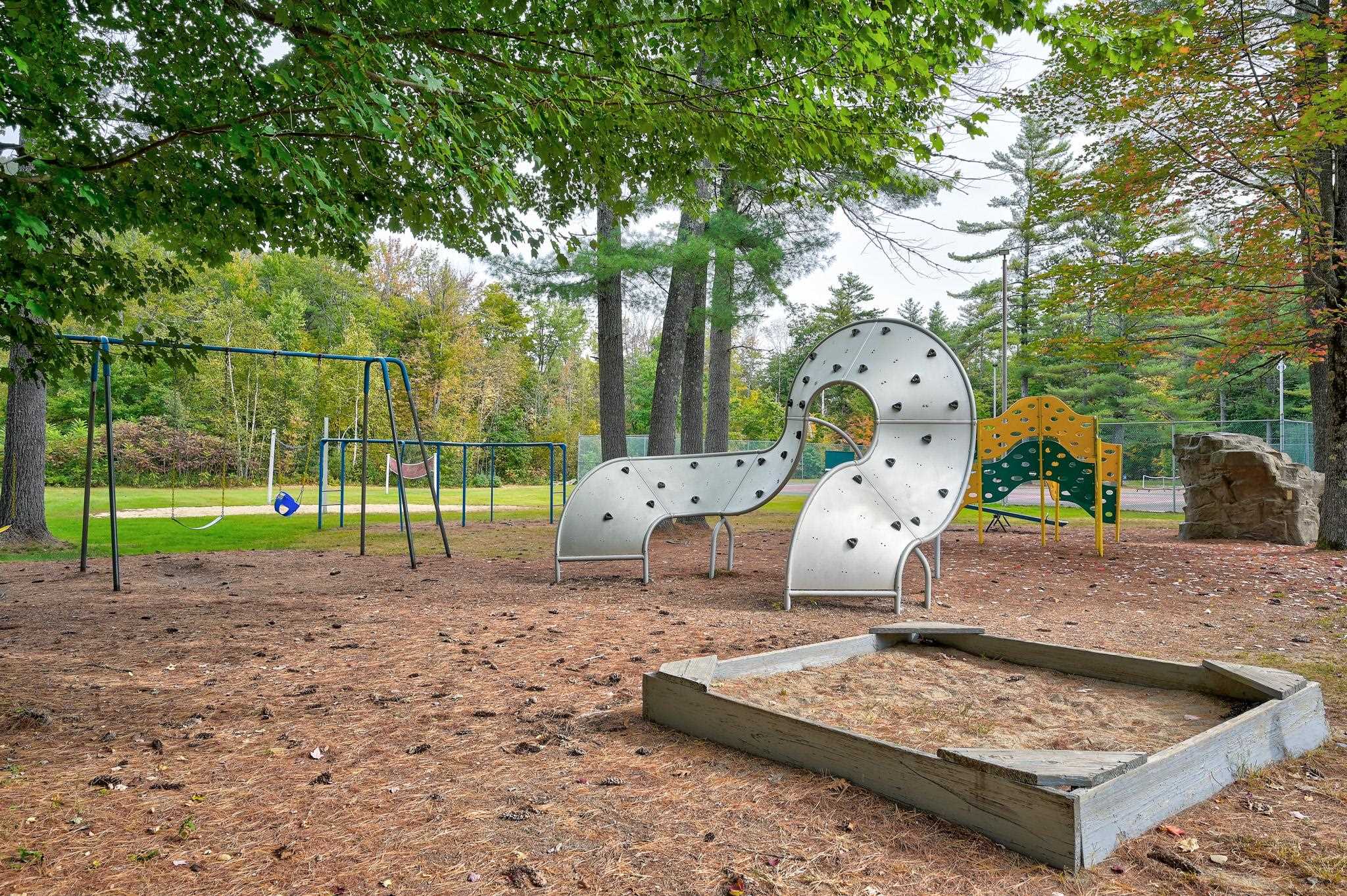 Wooded playground with swings, a curved climbing wall, play structure, and sandpit.