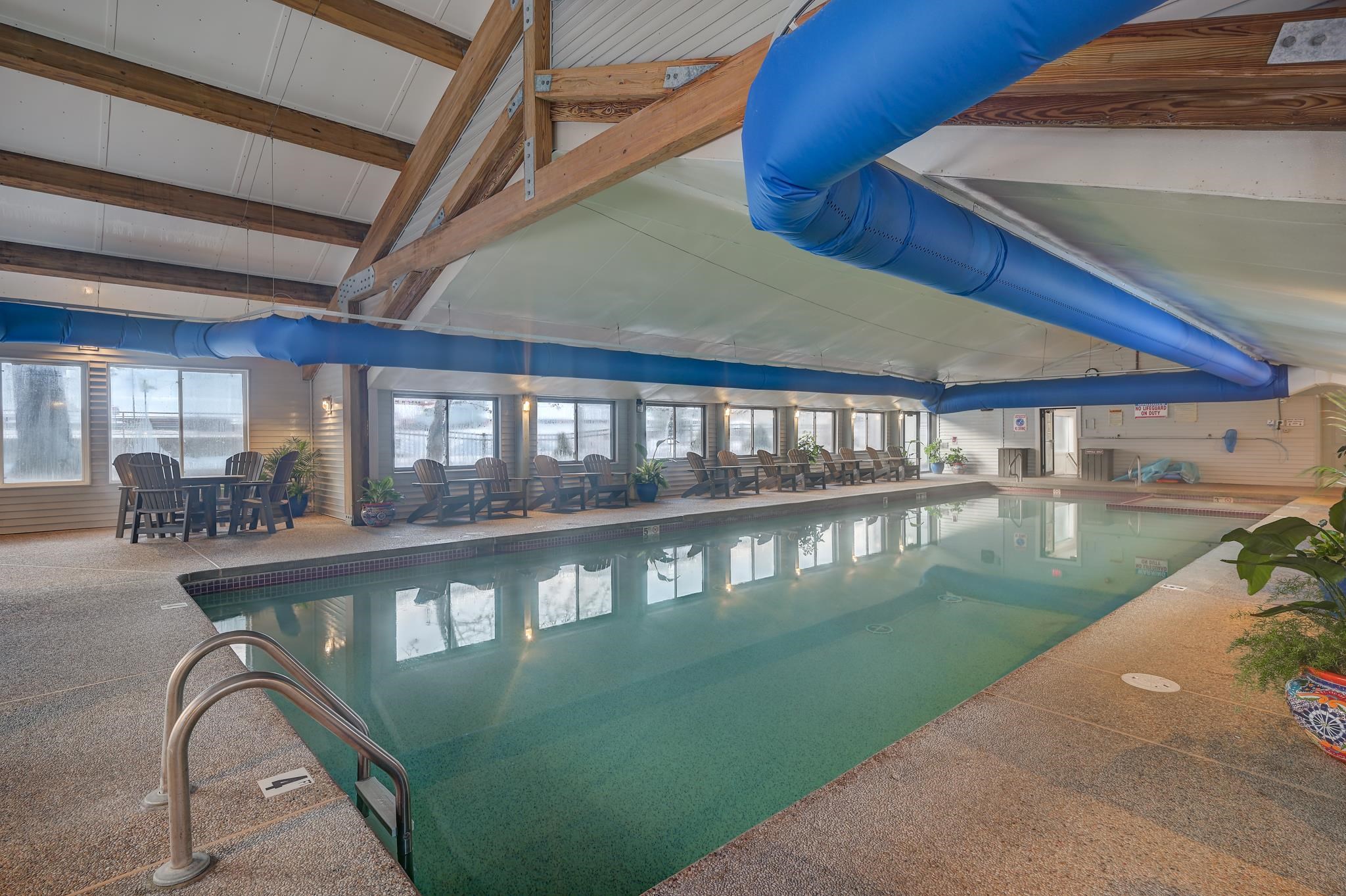 Indoor pool with blue ventilation ducts, exposed timber beams, and lounge chairs along the windows.