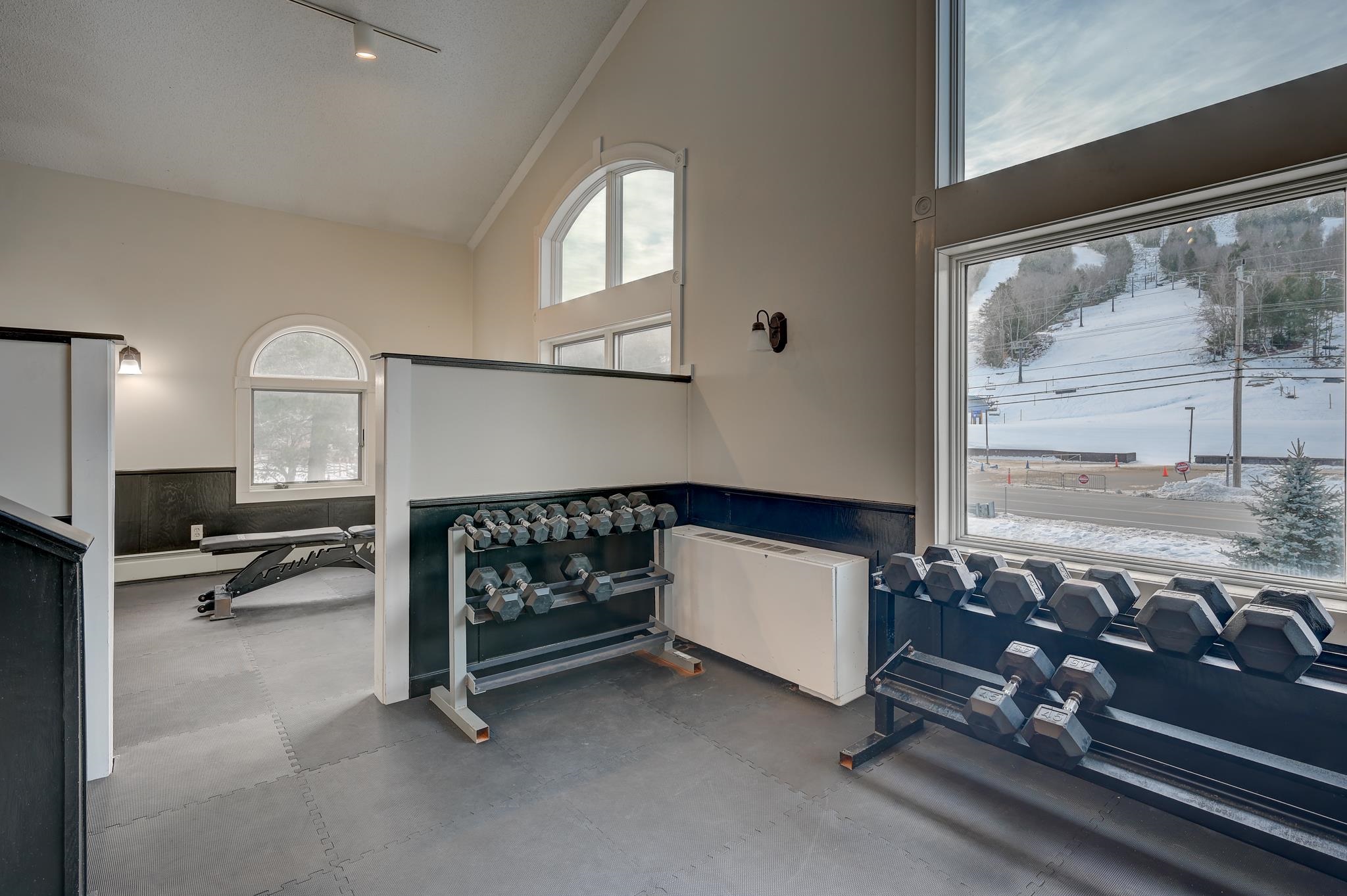Fitness room with dumbbell racks and a bench overlooking a snowy ski slope.