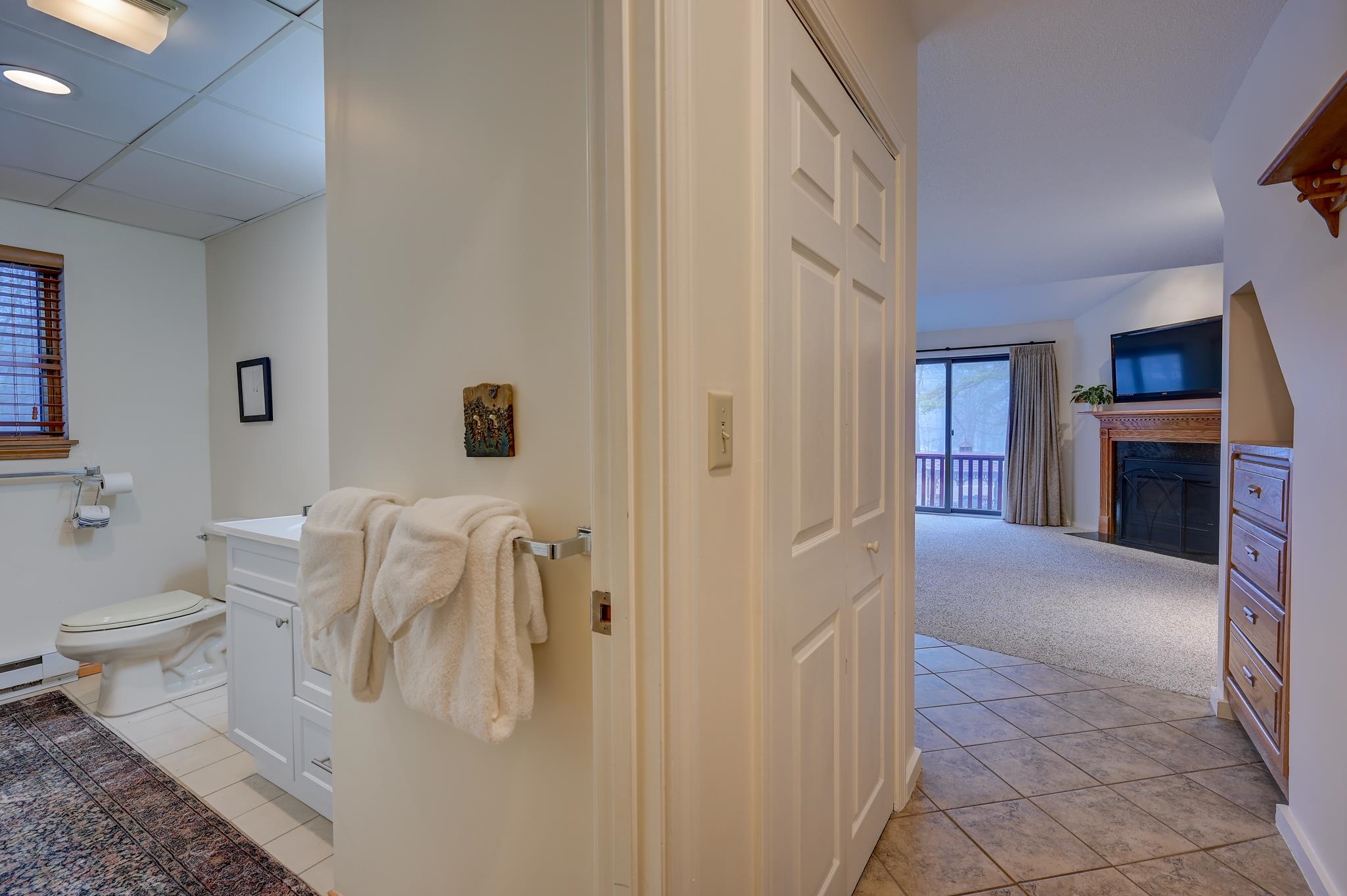 Bathroom opening to a living room with a fireplace and sliding glass doors to a balcony.
