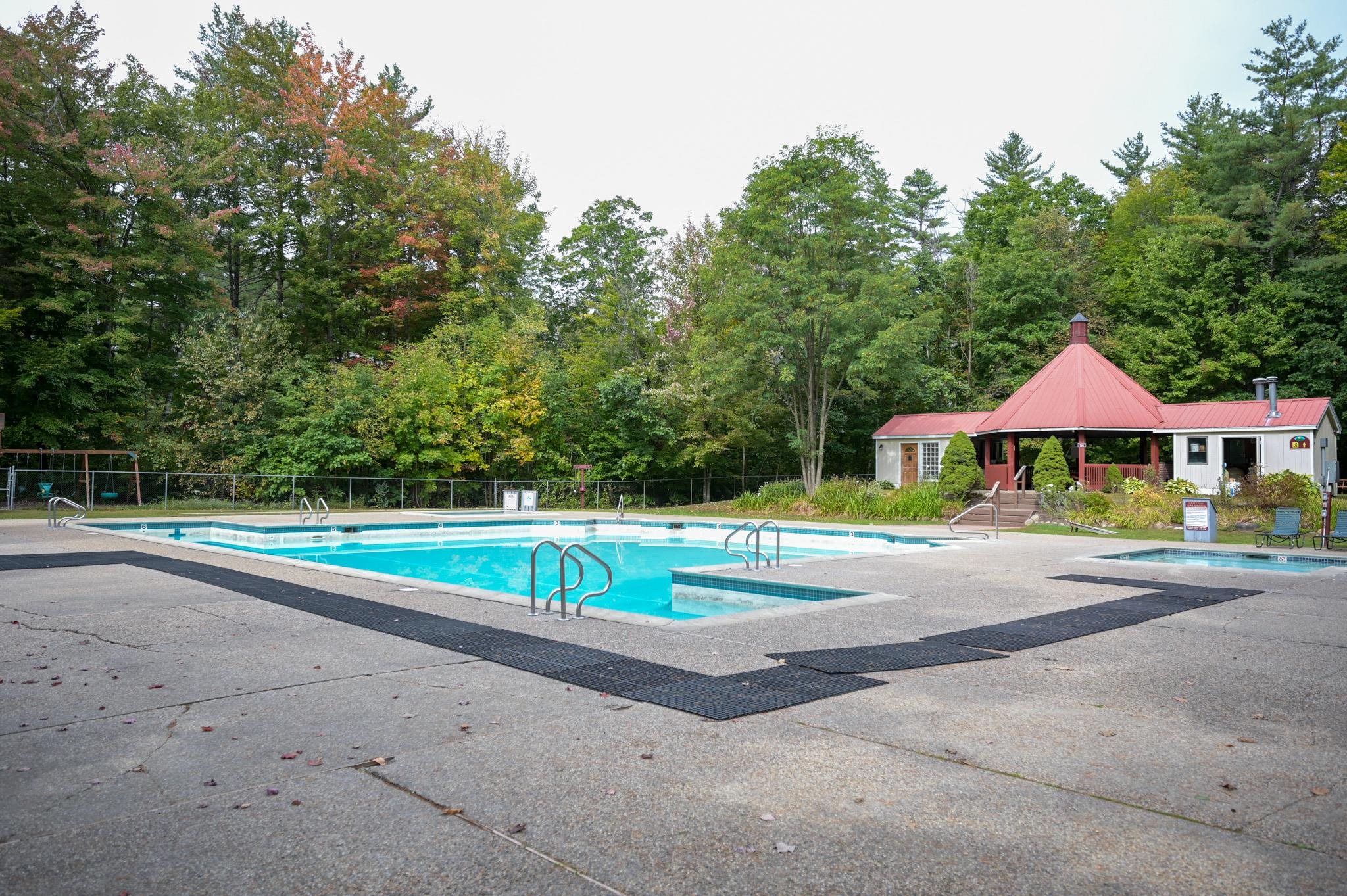 Outdoor pool and red-roofed pavilion surrounded by trees.