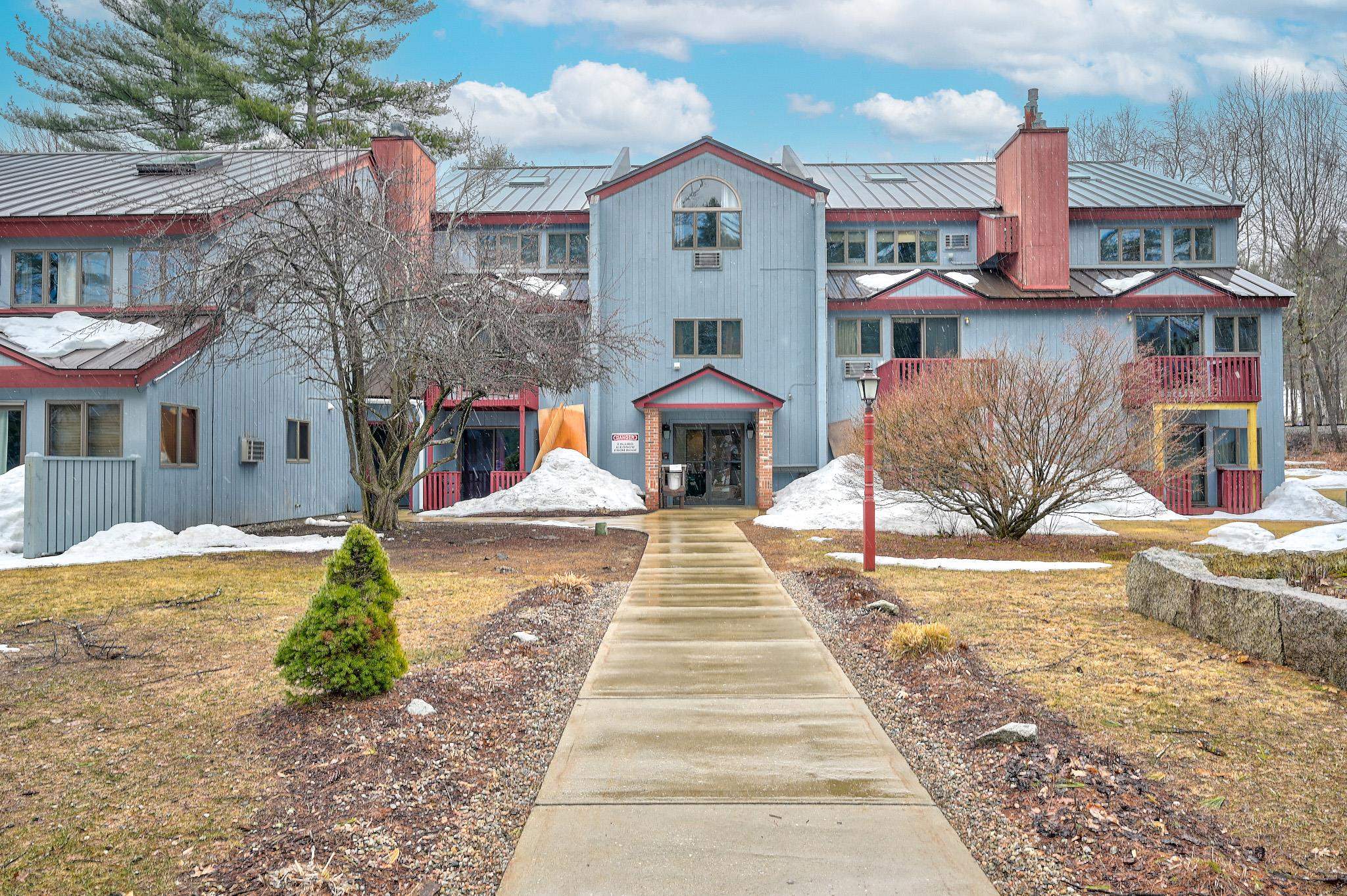 Condominium building with red-trimmed balconies and a walkway leading to the entrance.