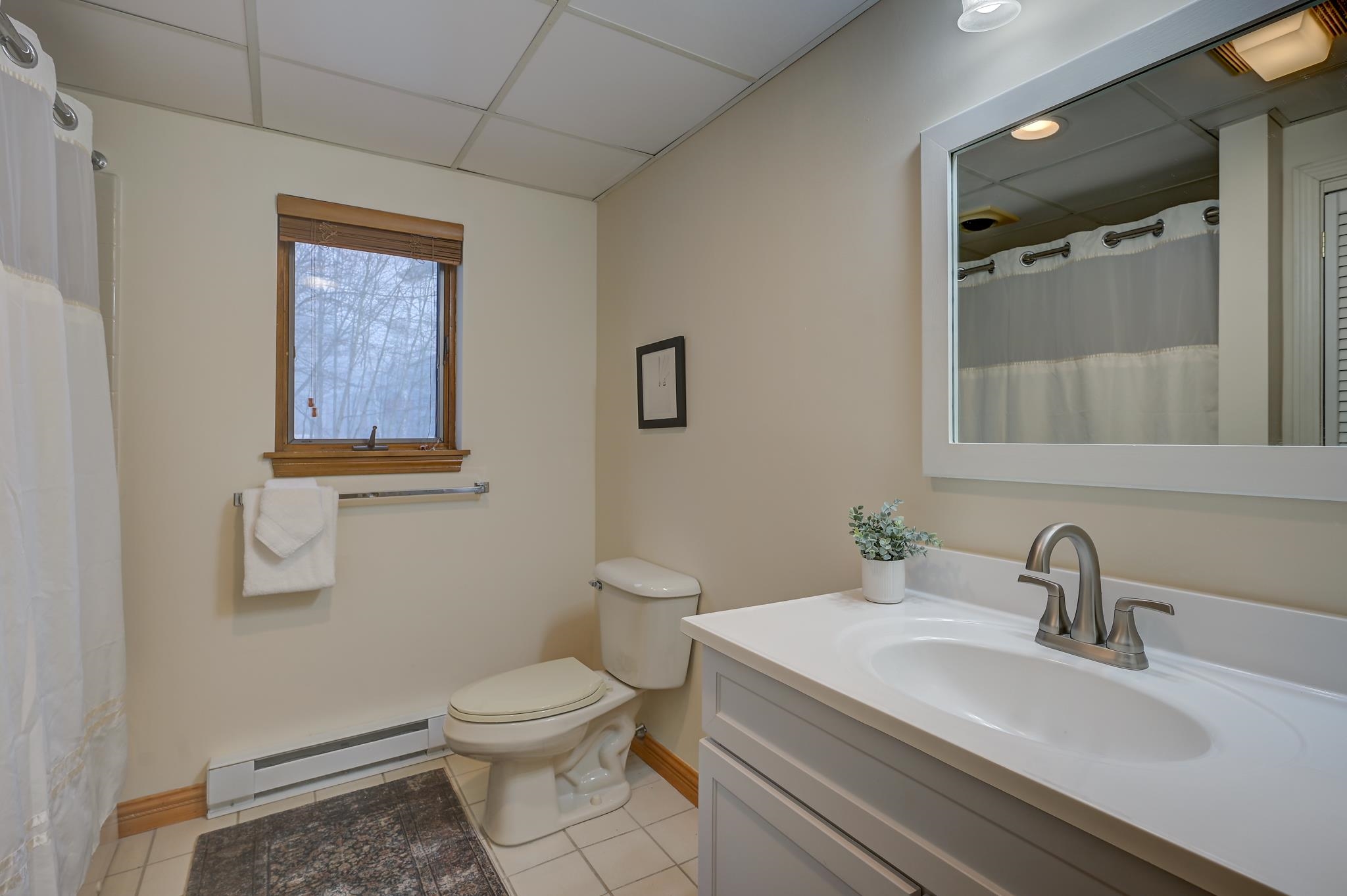 Bathroom with a white vanity, large mirror, toilet, and wood-trimmed window.