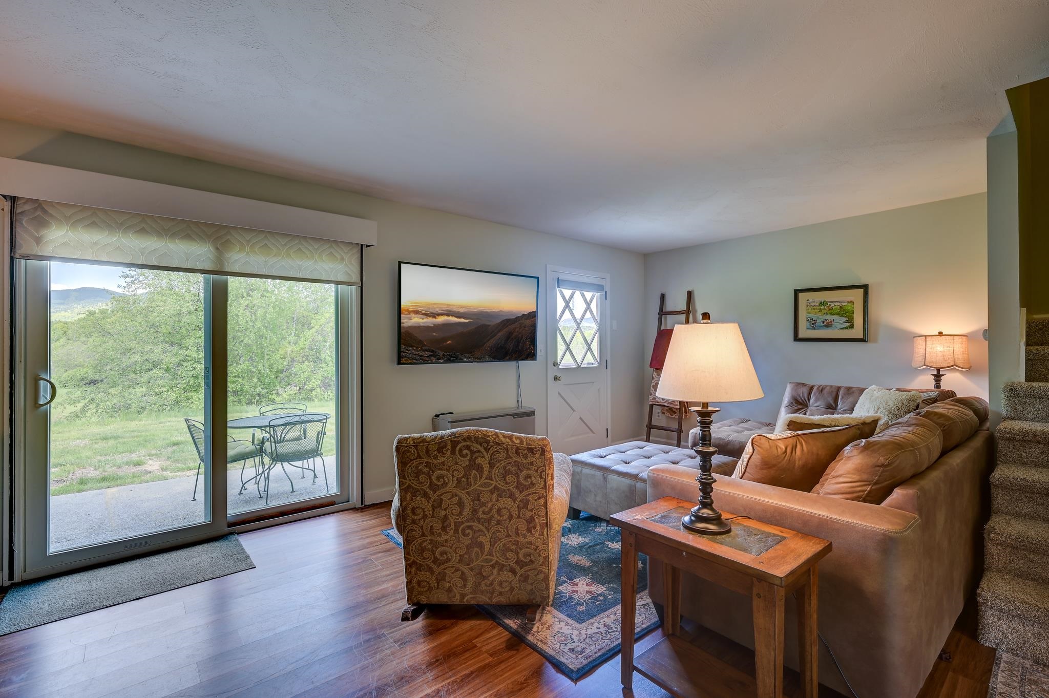 Living room with a brown sectional and patio doors overlooking green trees and distant hills.