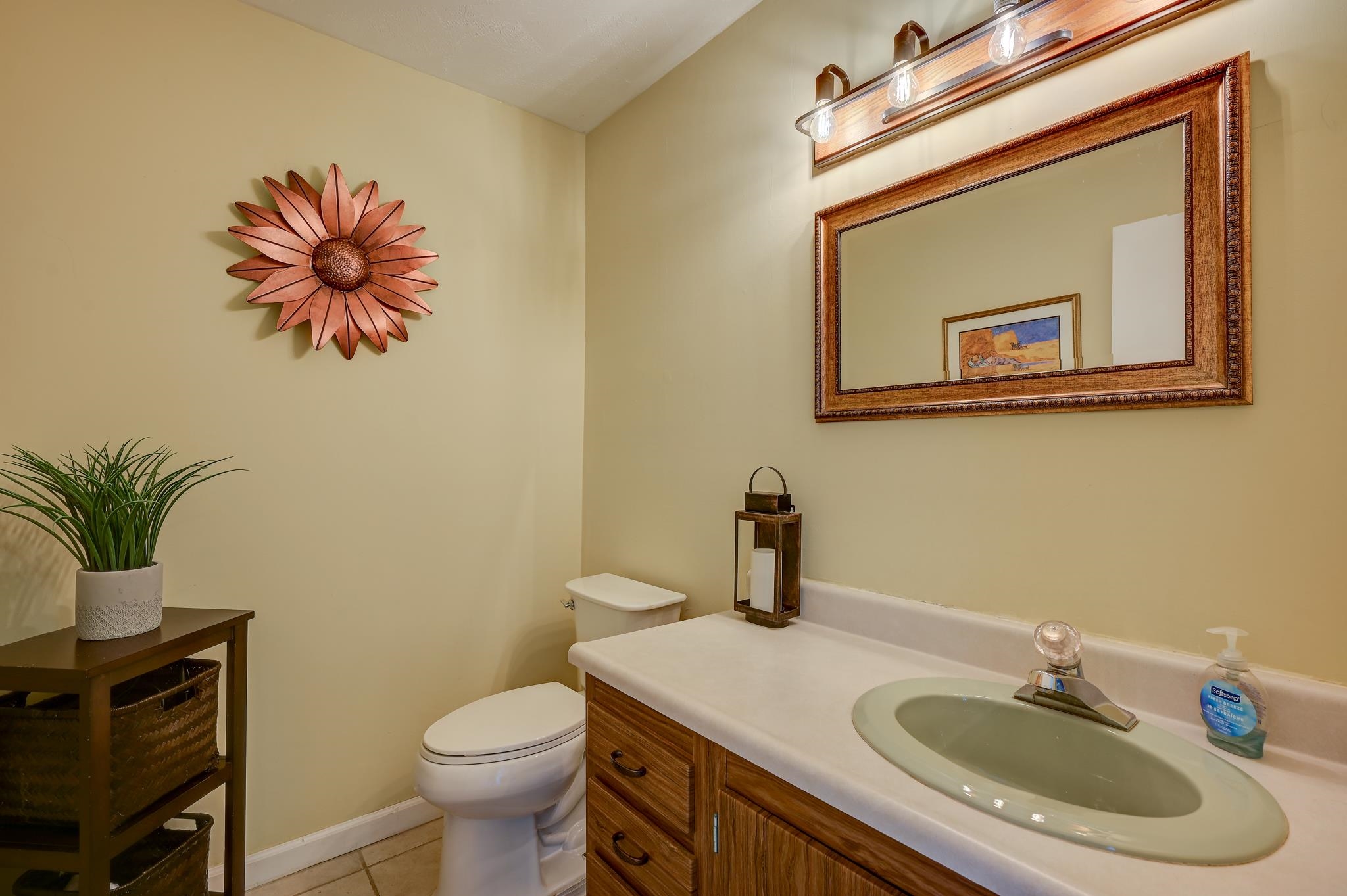 Bathroom with a wood vanity, pale green sink, large framed mirror, and sunflower wall decoration.