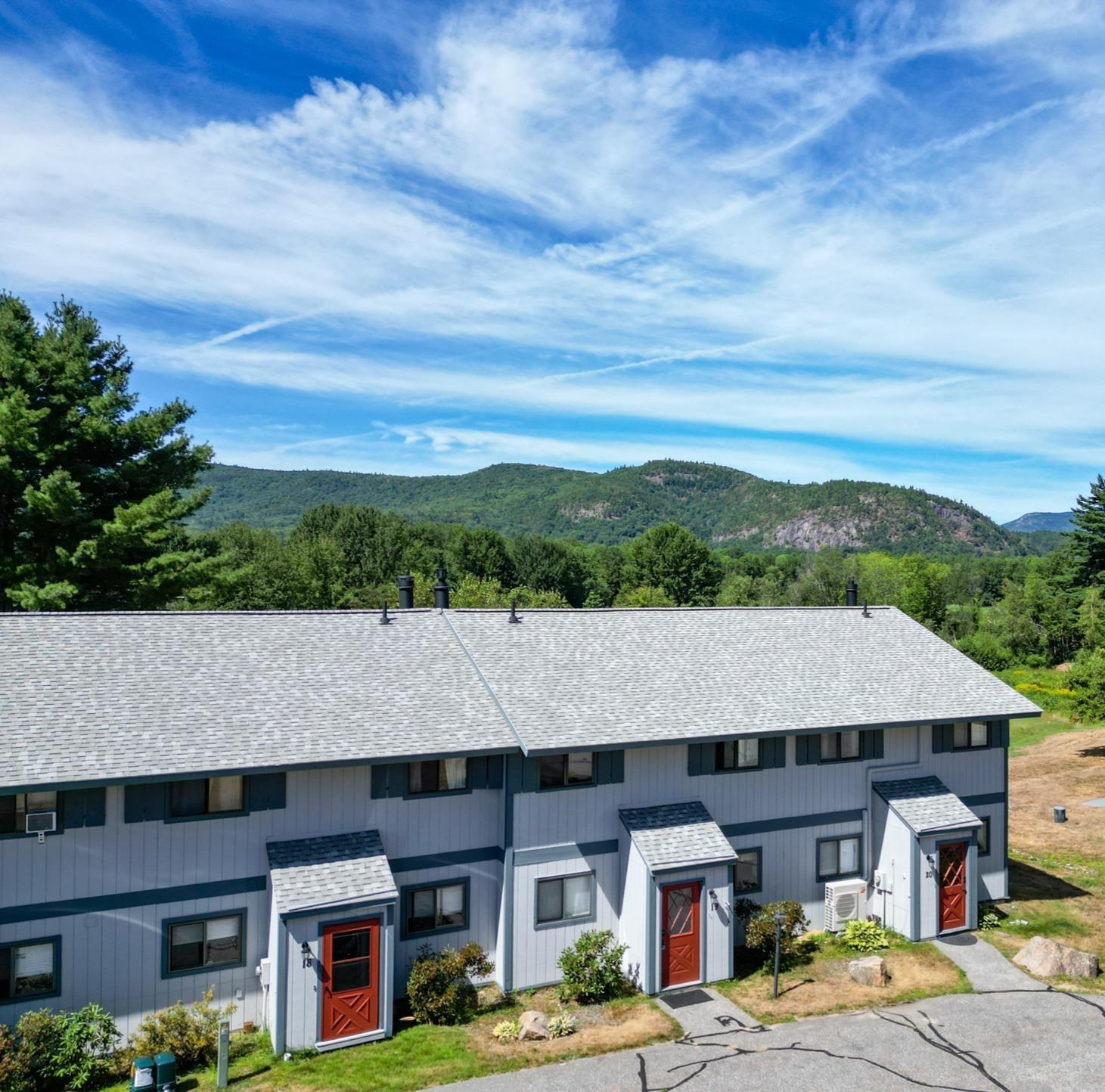 Gray condominium units with red doors stand below wooded mountain views.