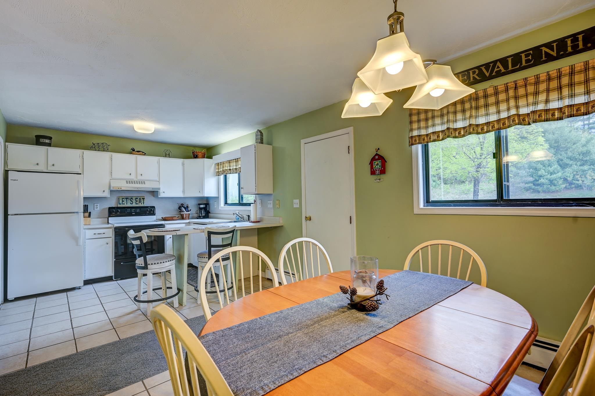 Kitchen and dining area with green walls, white cabinetry, breakfast counter, and wooden table by a large window.