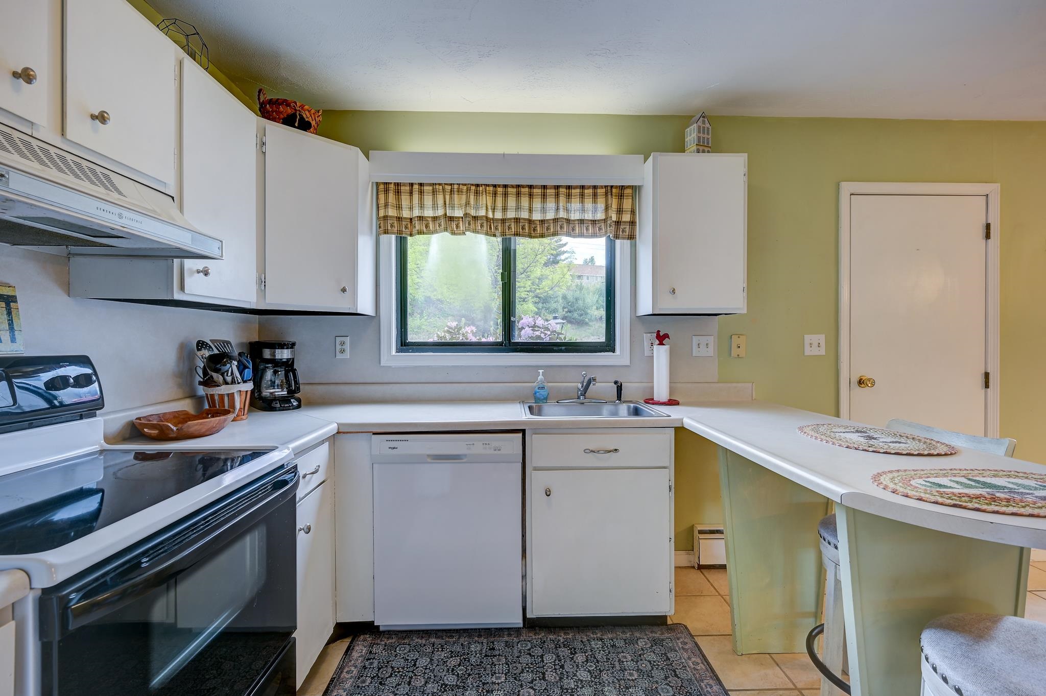 Kitchen with white cabinets, black range, sink beneath a garden-facing window, and a peninsula with stools.
