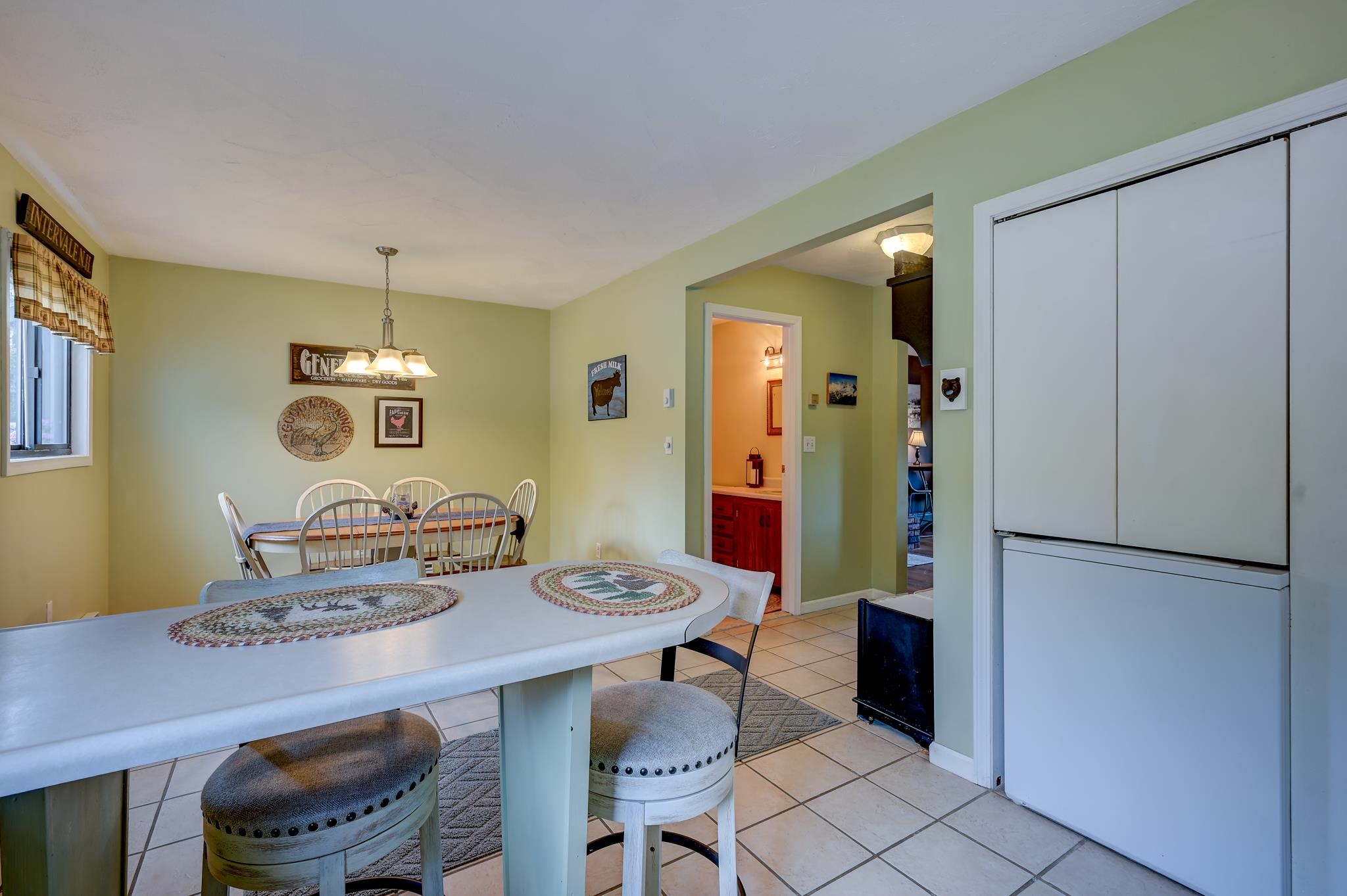 Kitchen dining area with a white table, tiled floor, and large refrigerator.