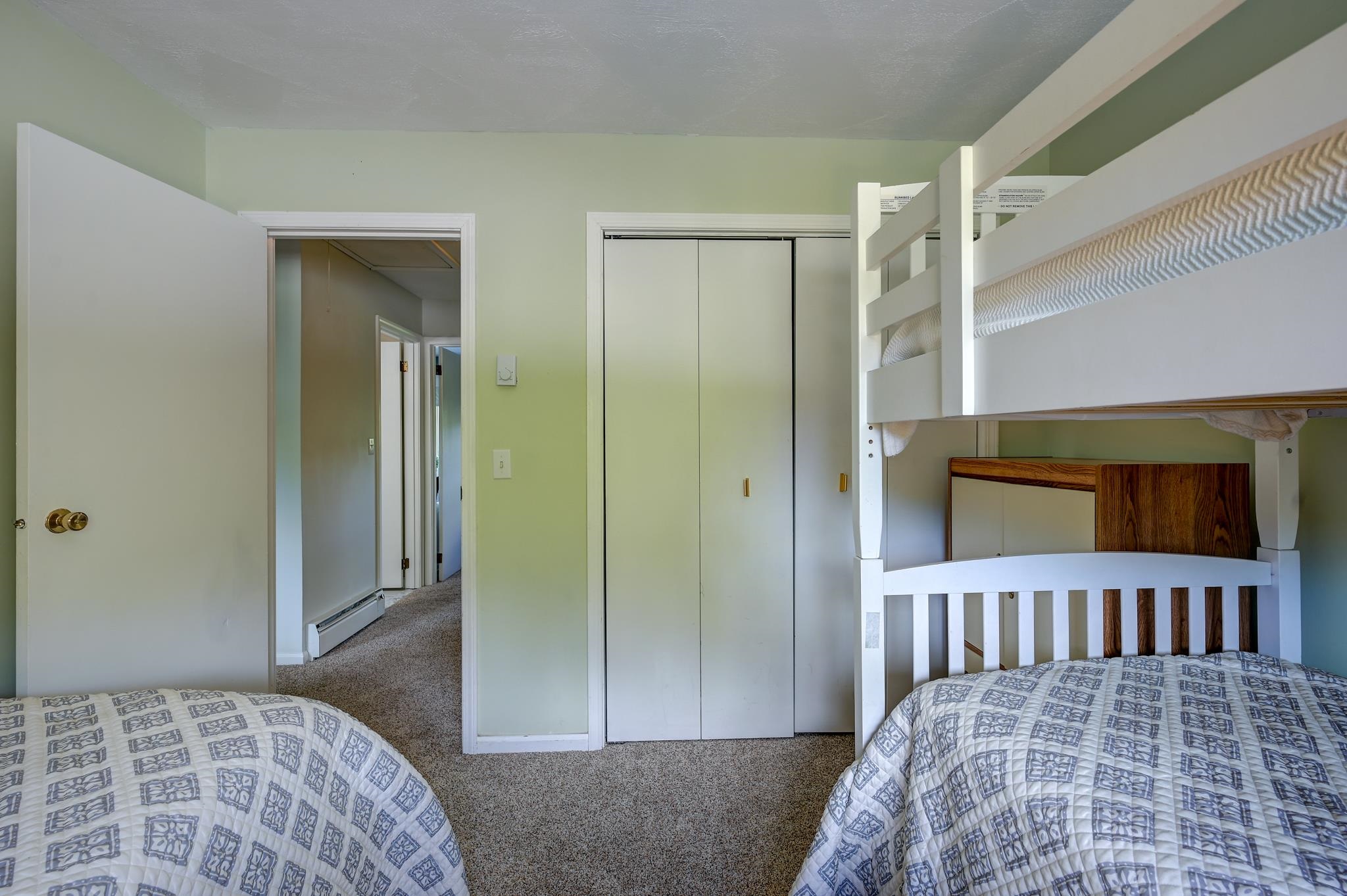 Bedroom with two twin beds, a white bunk bed, patterned quilts, and a sliding-door closet.