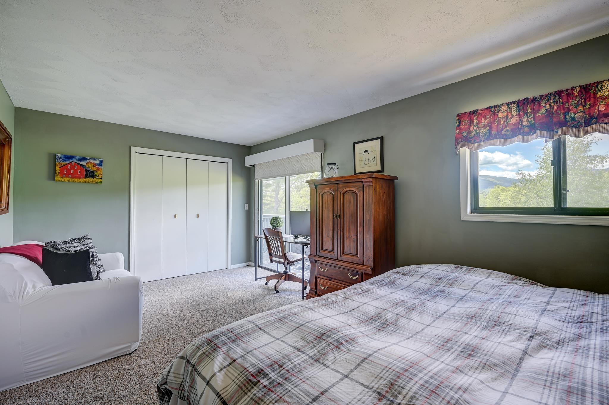Furnished bedroom with a plaid bedspread, wooden armoire, and mountain views through the window.