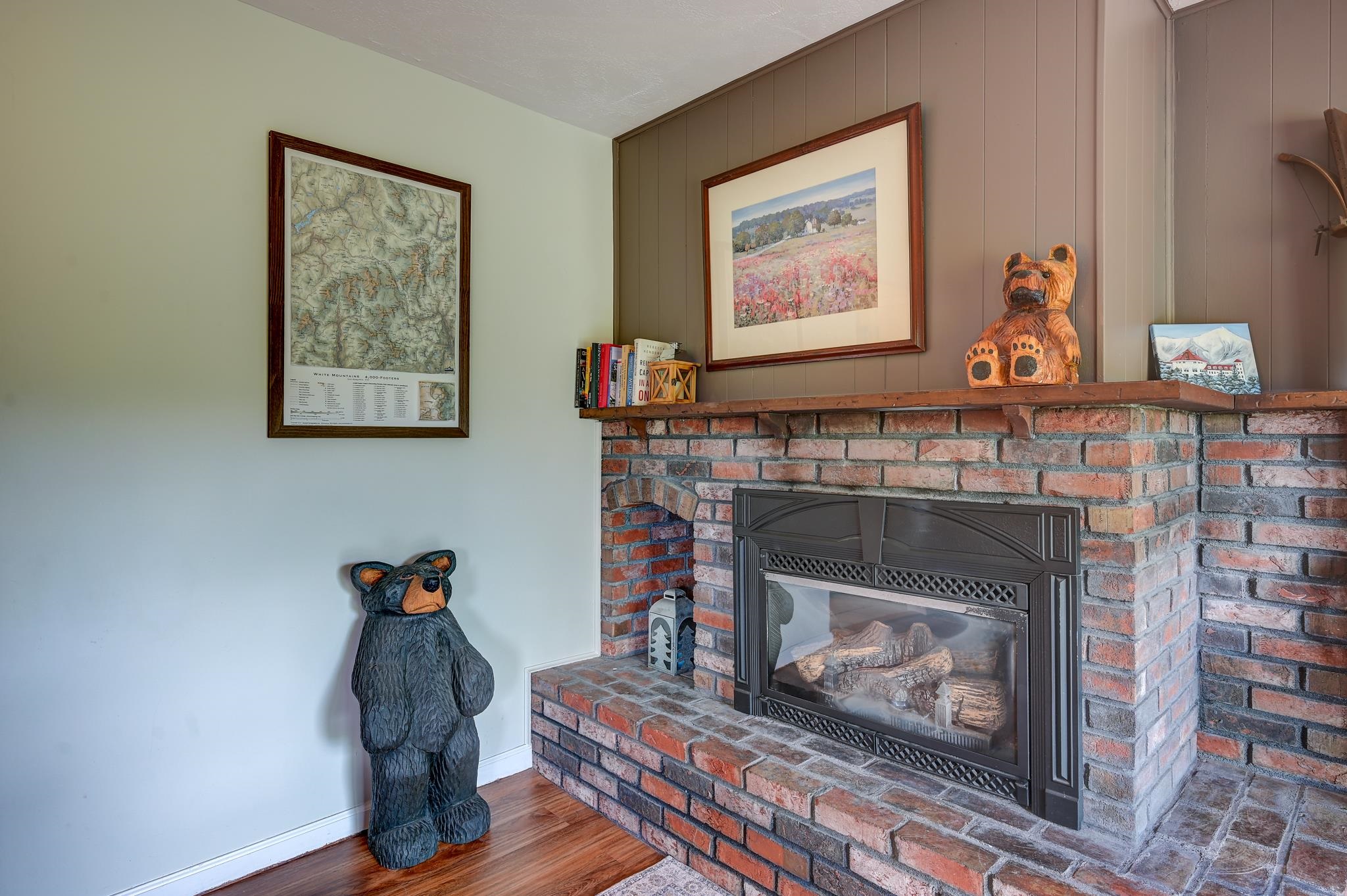 Living room with a brick fireplace, glass-front insert, carved bear figures, and framed wall art.